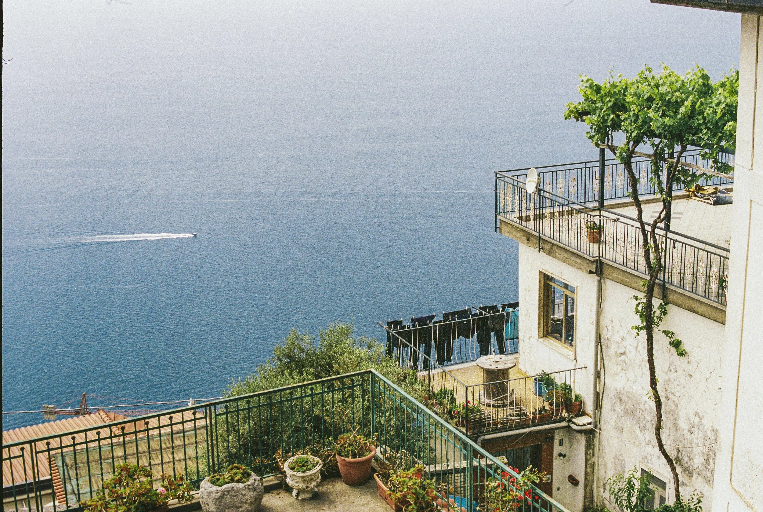 Balcony with potted plants overlooking blue sea and a boat passing by.