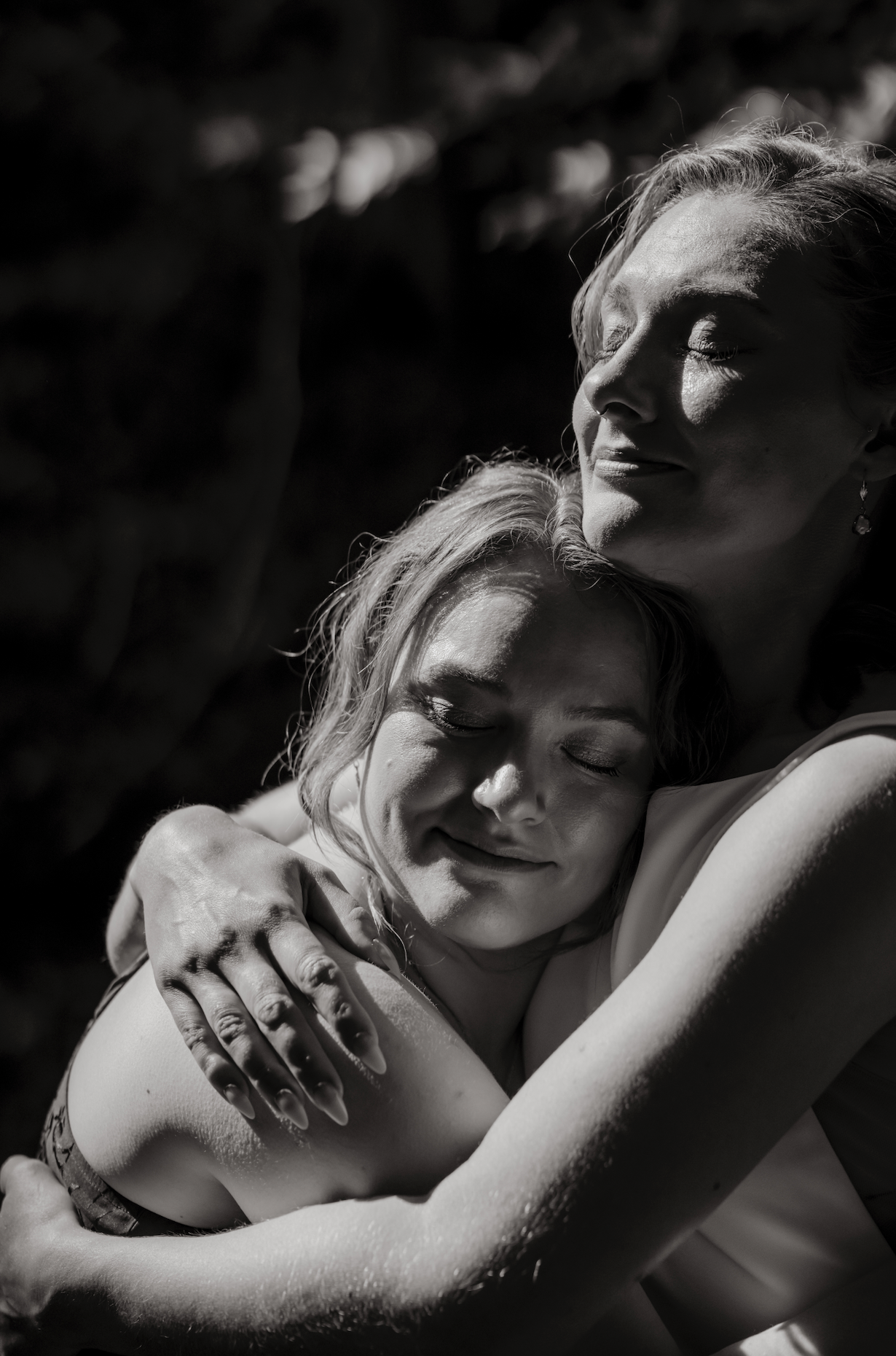 Black and white photo of two women embracing, with their eyes closed and peaceful expressions, showing emotional connection and comfort.