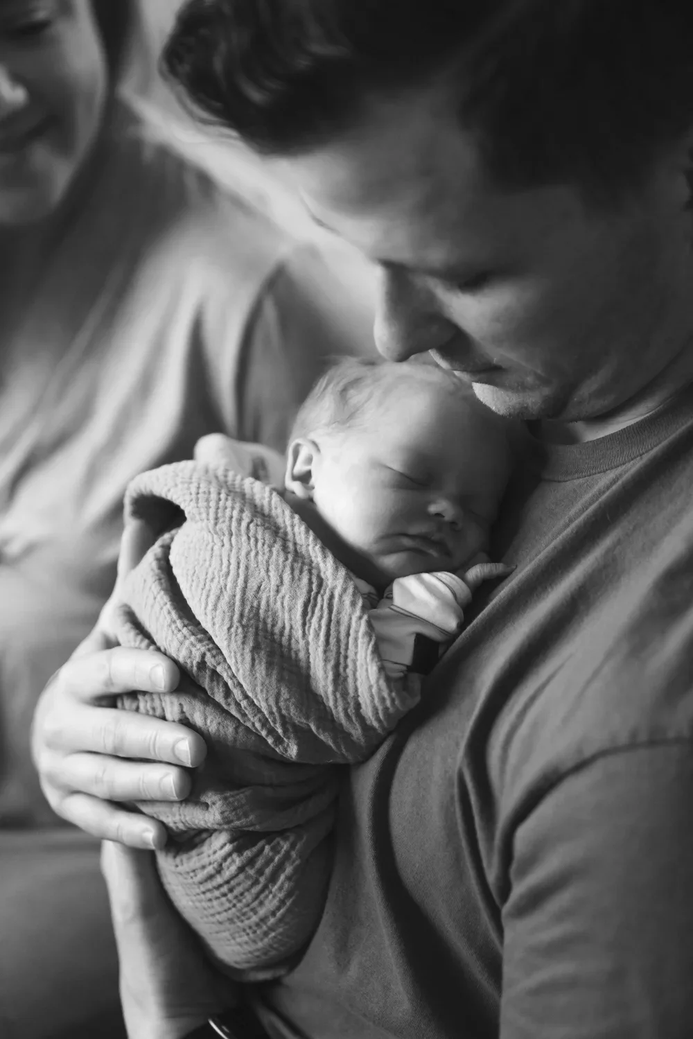 A man holding a sleeping newborn baby in his arms, close-up shot in black and white.