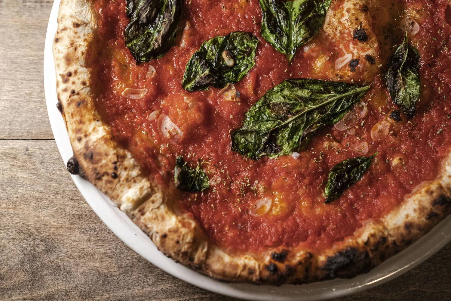 Close-up of a pepperoni pizza with basil leaves on top, on a white plate on a wooden surface.