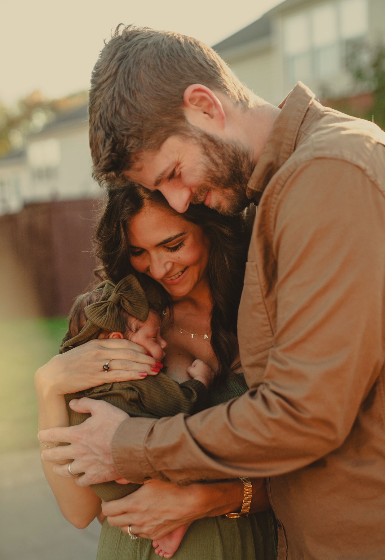 Family of three, parents and their baby, sharing a joyful and intimate moment outdoors during sunset.