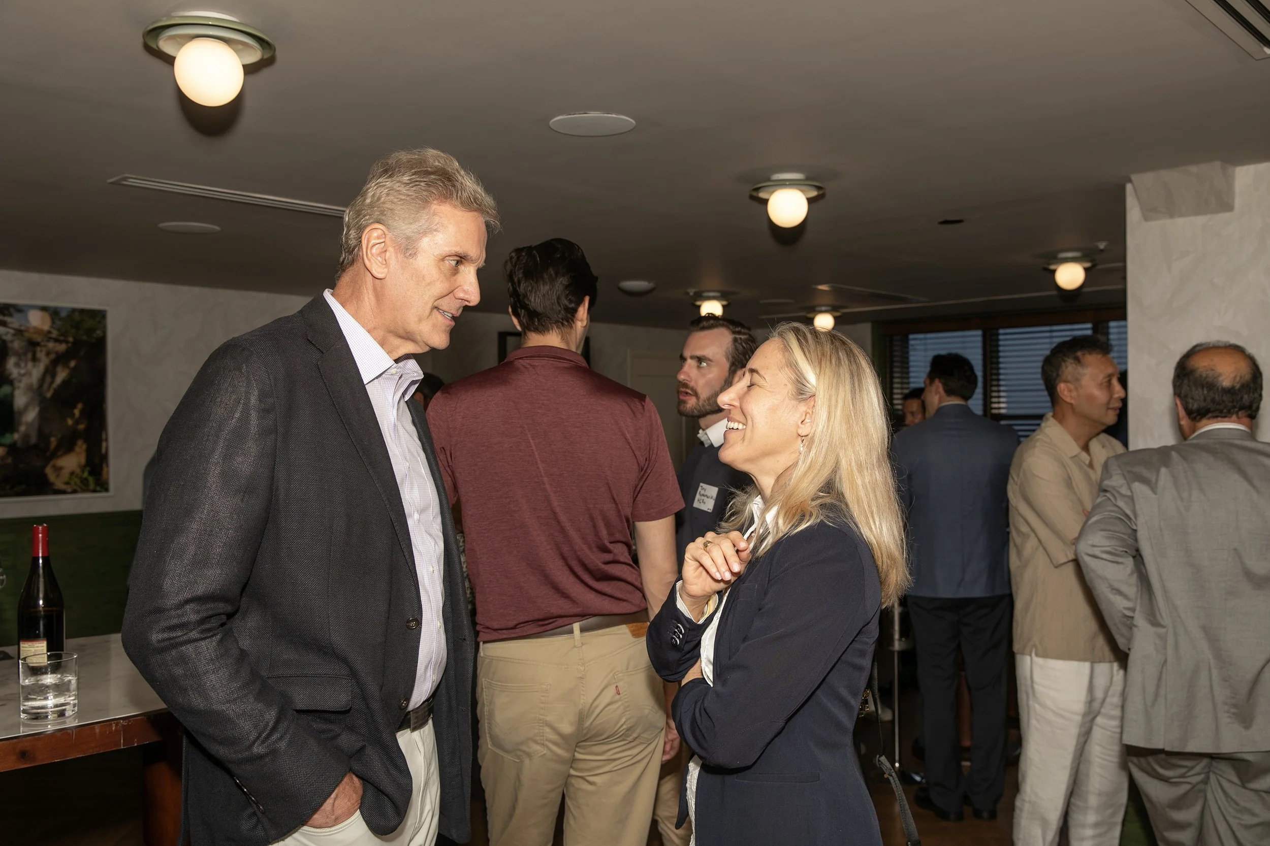 A group of professionally dressed men and women socializing at an indoor gathering, engaging in conversation.