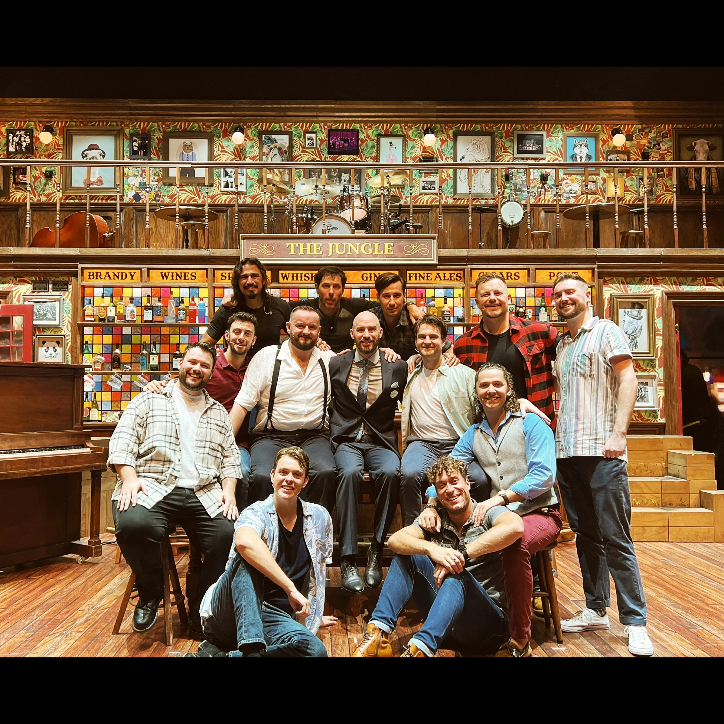 Group of people posing for a photo in a restaurant with colorful artwork and framed photos on the wall behind them.