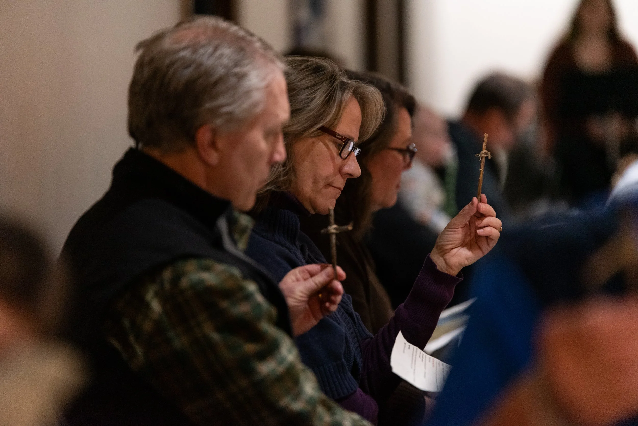 People sitting in a row holding prayer sticks during a religious ceremony.