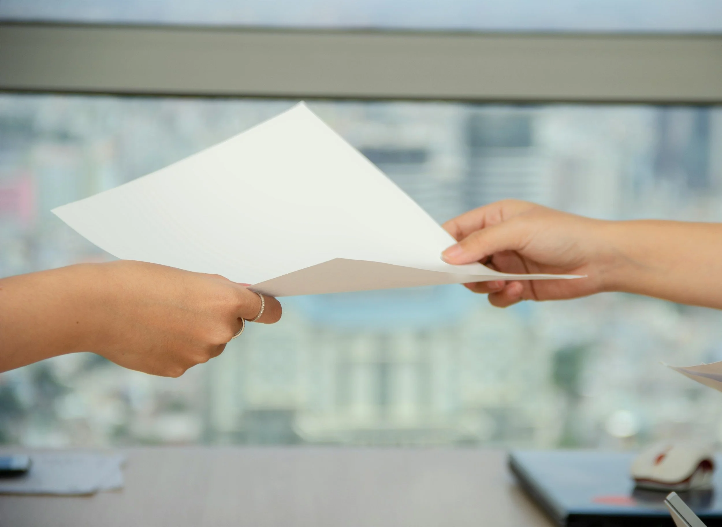 Two people exchanging a white piece of paper, with a background of kitchen appliances and ceramics on a countertop.