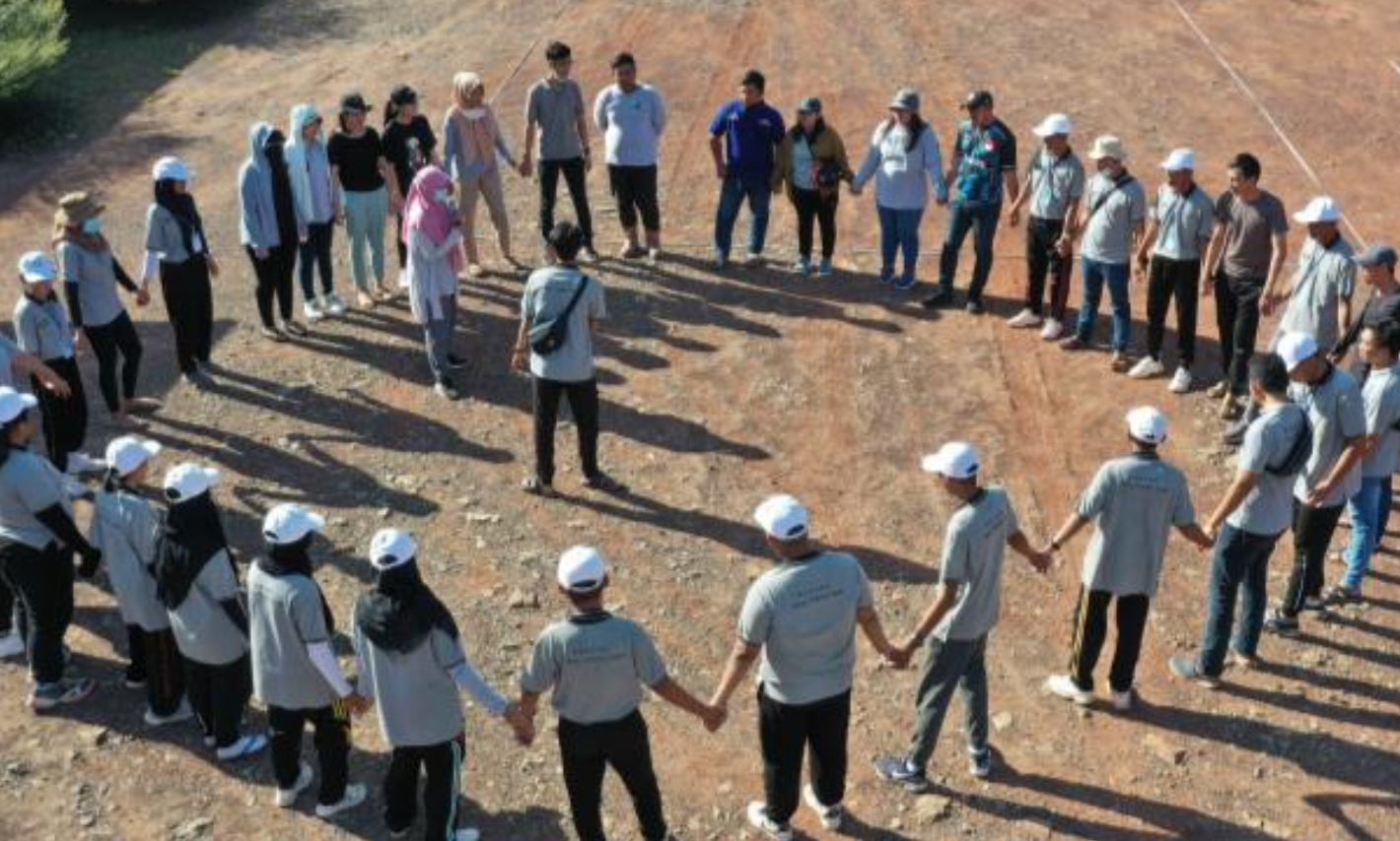 Group of people holding hands in a circle outdoors on a sunny day.