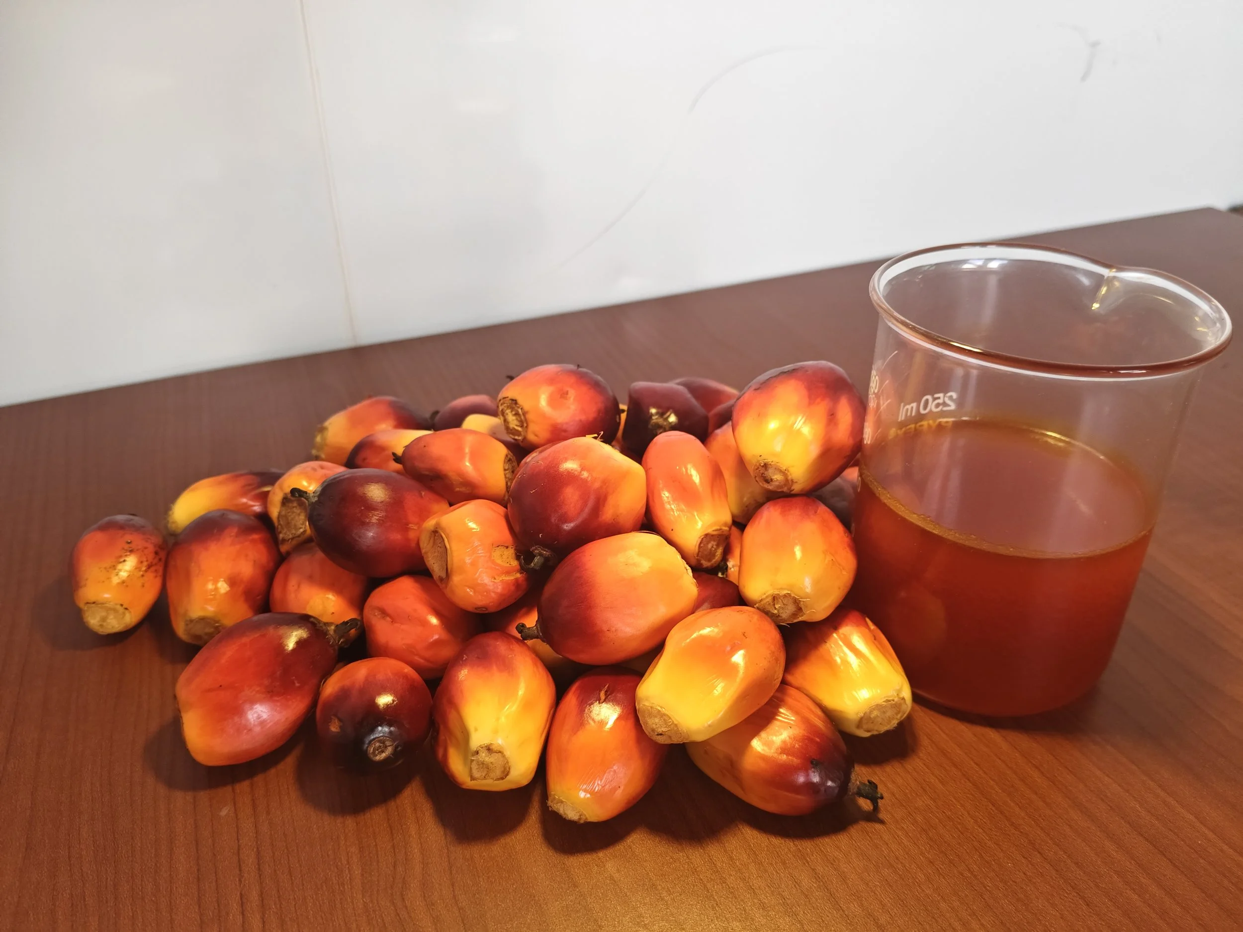 A glass of tea next to a pile of ripe red and yellow palm fruits on a wooden surface.