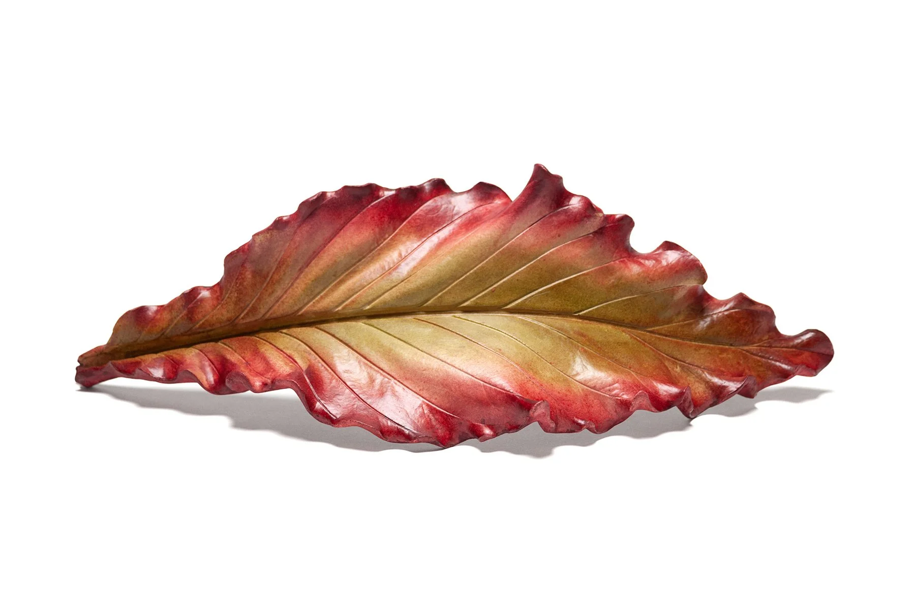 A single colorful autumn leaf sculpture with shades of red, orange, and yellow against a white background.