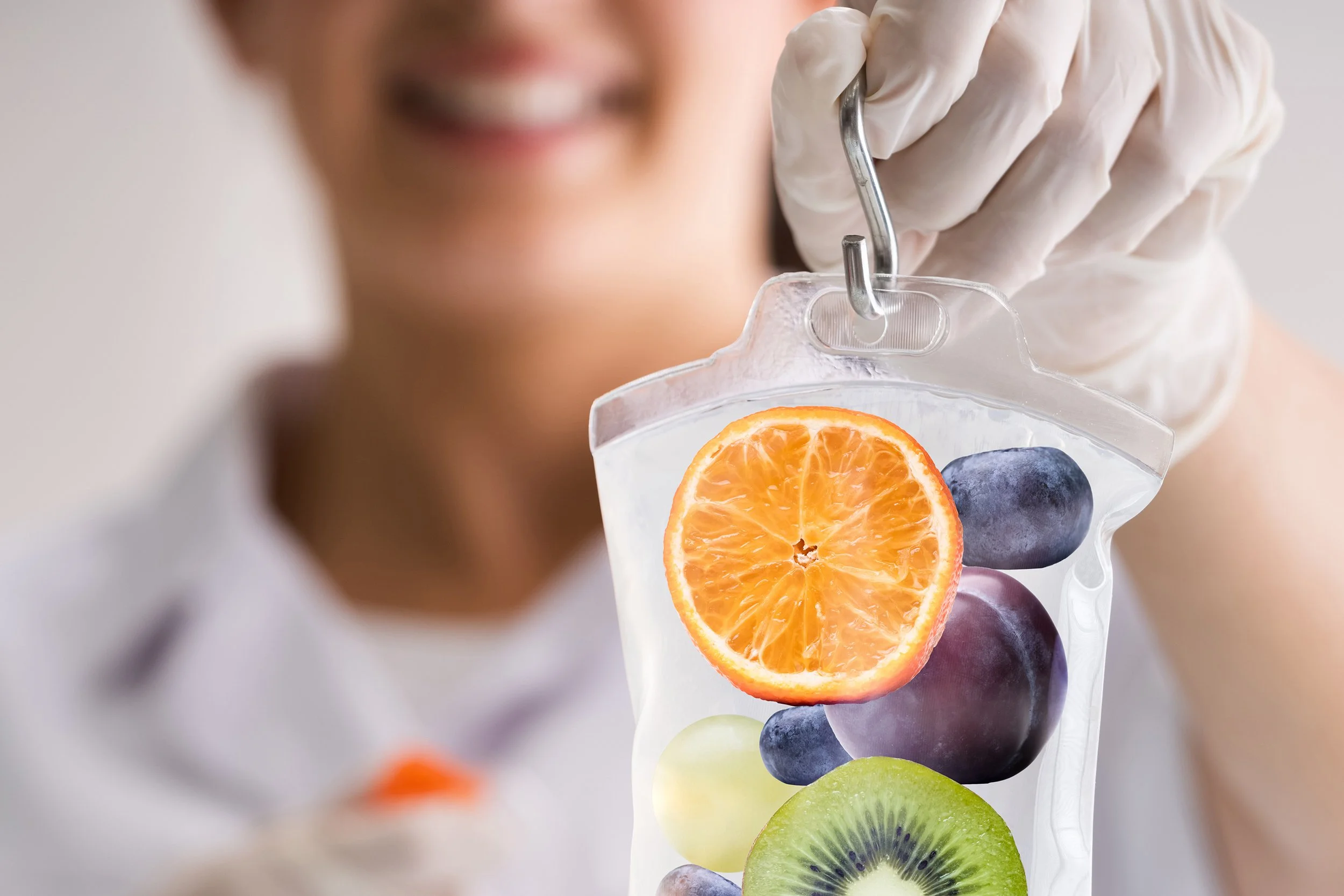 A woman in medical gloves holds a transparent bag with sliced orange, kiwi, grapes, and blueberries inside.