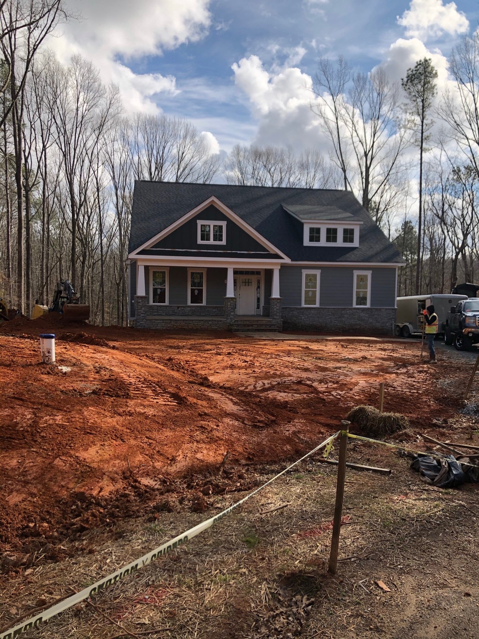 Construction site in front of a house with unfinished yard, dirt ground, caution tape, and a person standing nearby.