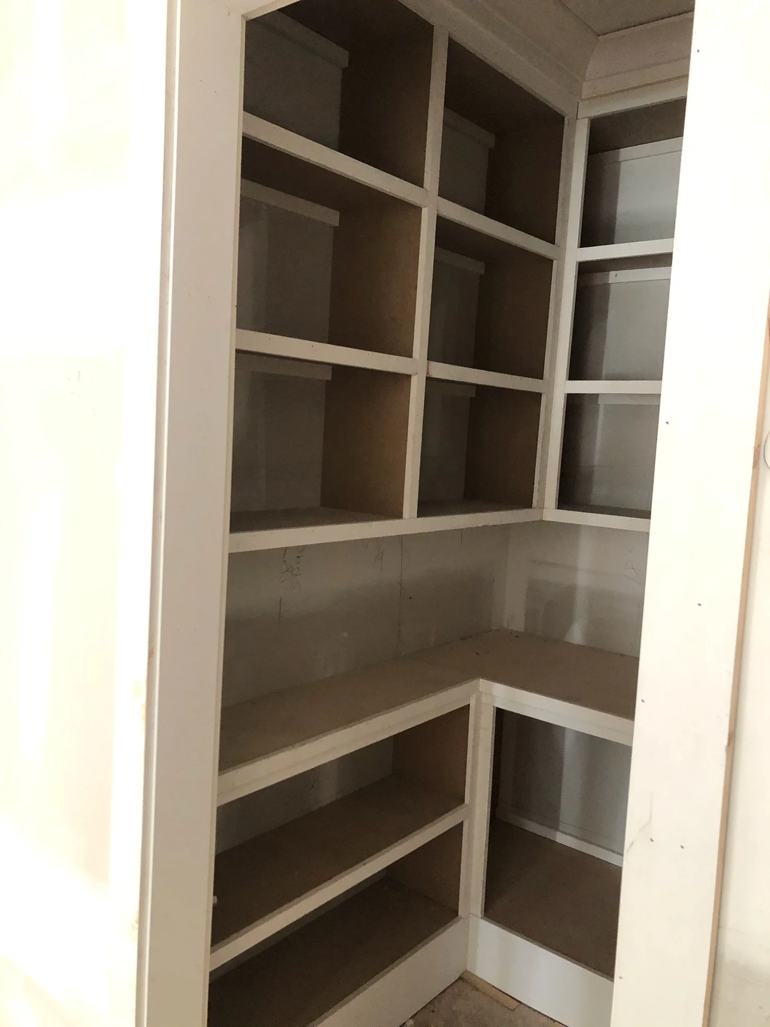 Empty kitchen cabinet with multiple shelves, some with slanted surfaces for storing bottles or cans.