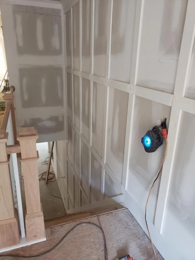 Interior view of a staircase with unfinished framing on the wall, with a construction light plugged into the wall.