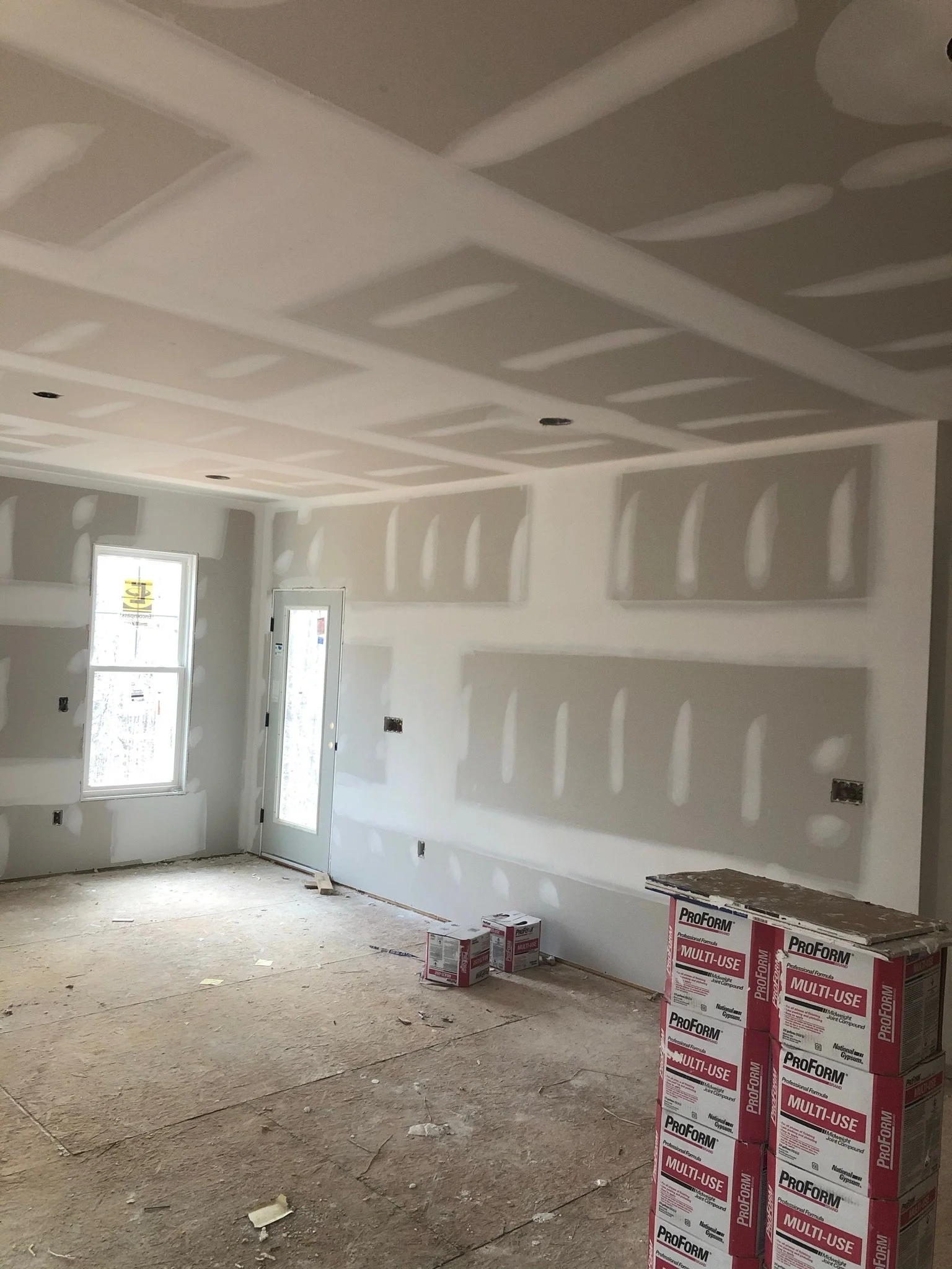 Interior room under construction with unfinished drywall and insulation. There are windows and open wall spaces, with boxes of ProForm multi-use joint compound on the floor.