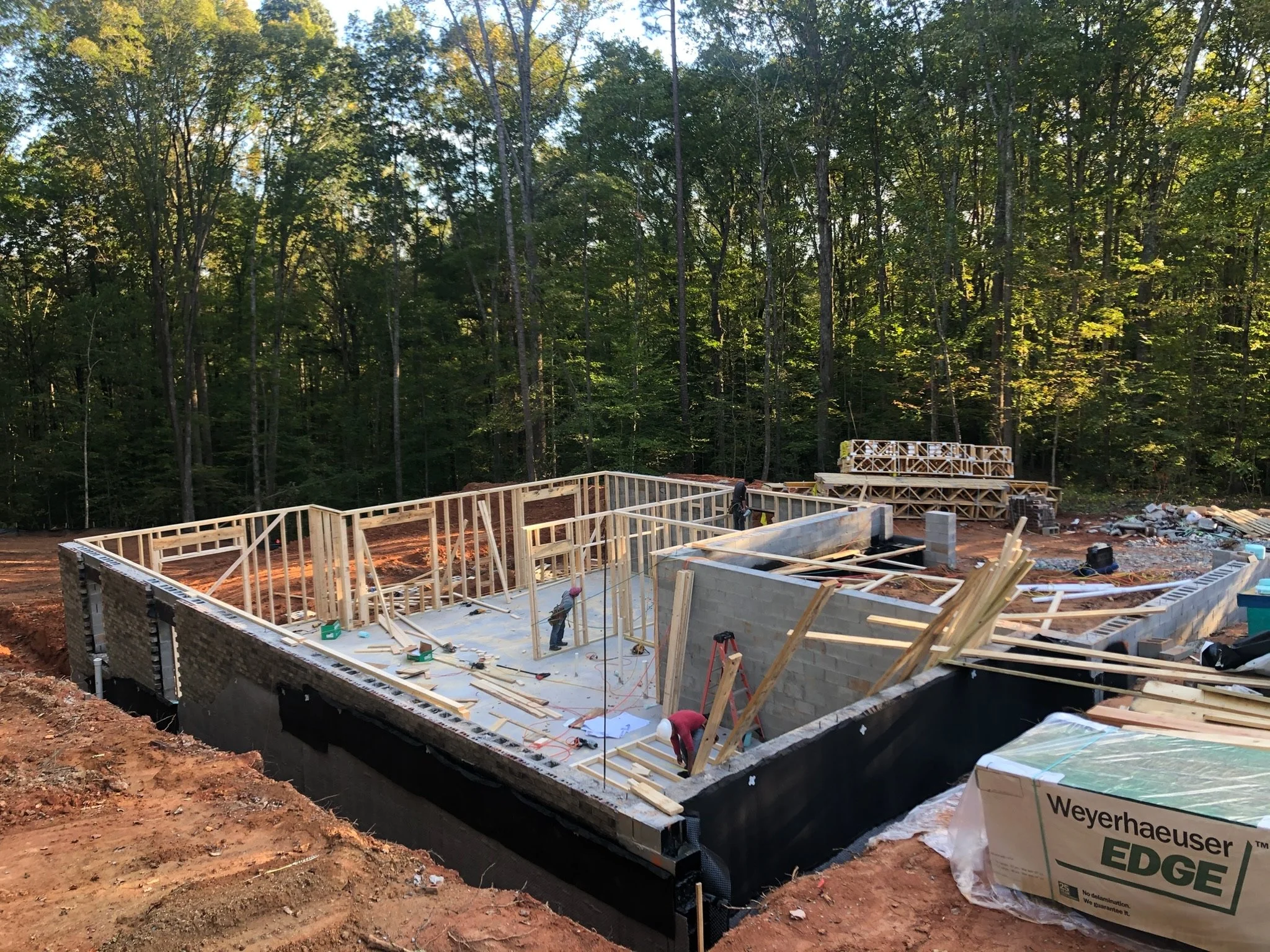 Construction site with a wooden frame of a building in progress, surrounded by trees and equipment.