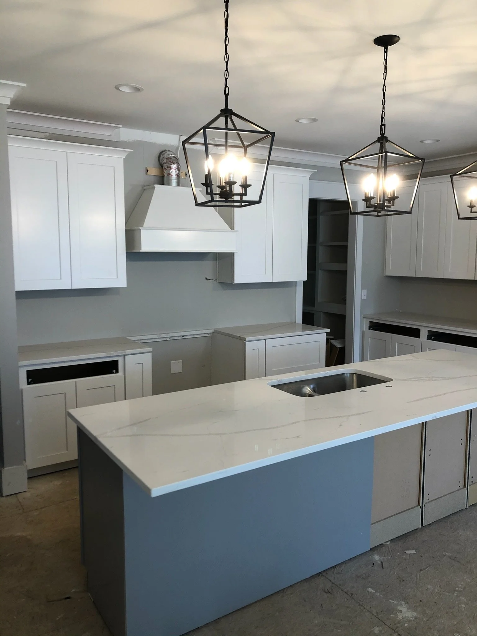 A kitchen with white cabinets, a kitchen island with a white marble countertop, and three modern geometric black pendant lights hanging from the ceiling.