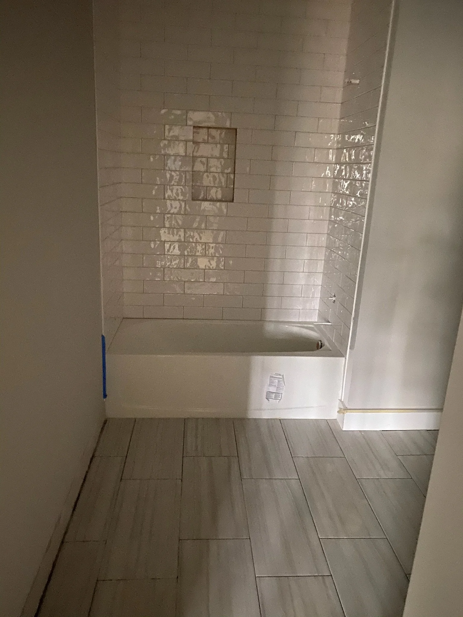 Photo of an unfinished room with tan tiled walls and floor, and a partially installed shower stall with a small opening in the wall for plumbing.