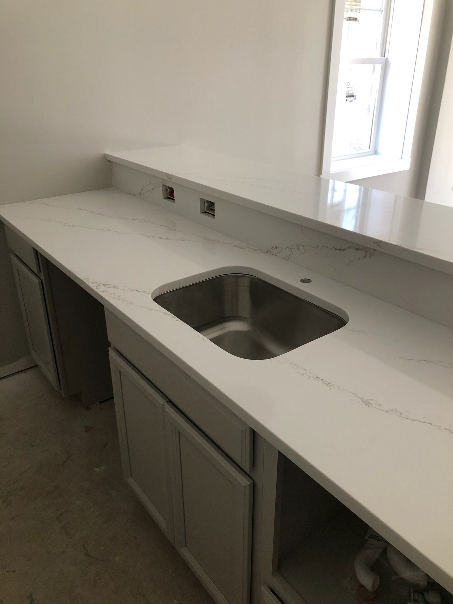 Empty kitchen countertop with a built-in sink and electrical outlets near a window.