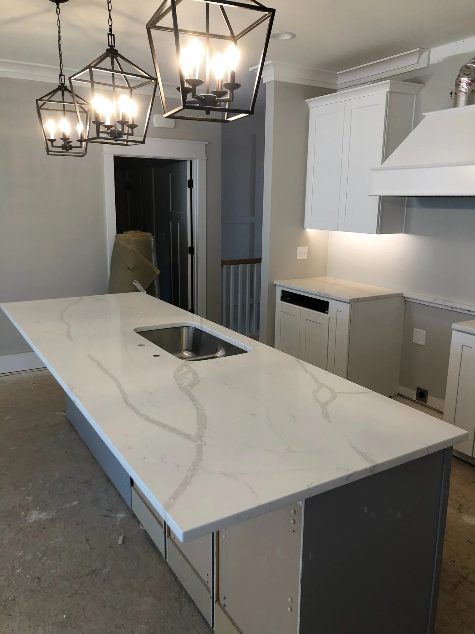 White kitchen island with a marble pattern countertop and a built-in sink, in a partly finished and unfurnished kitchen