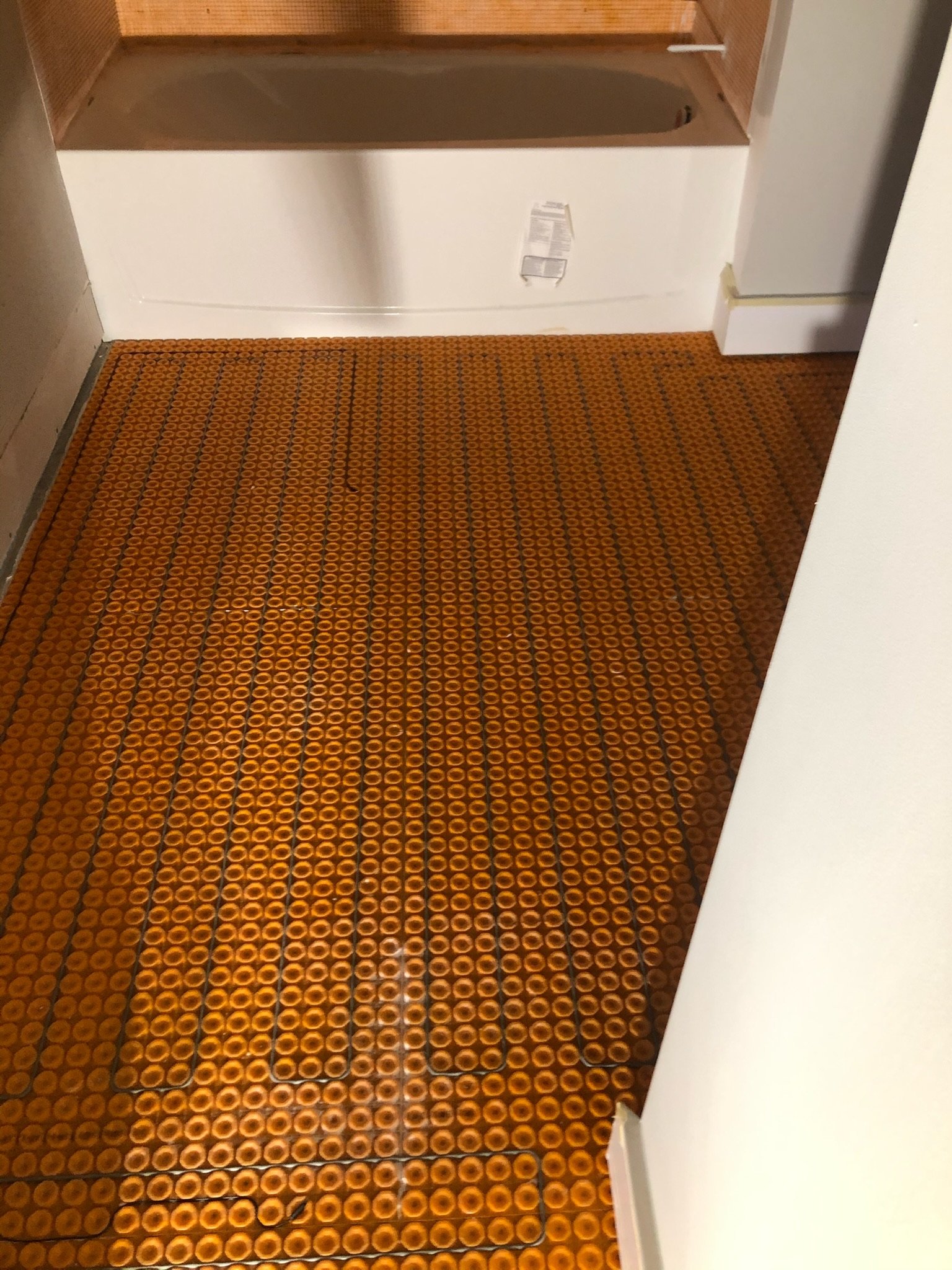 View of a corridor with orange patterned flooring and white walls, with part of a kitchen or room in the background.