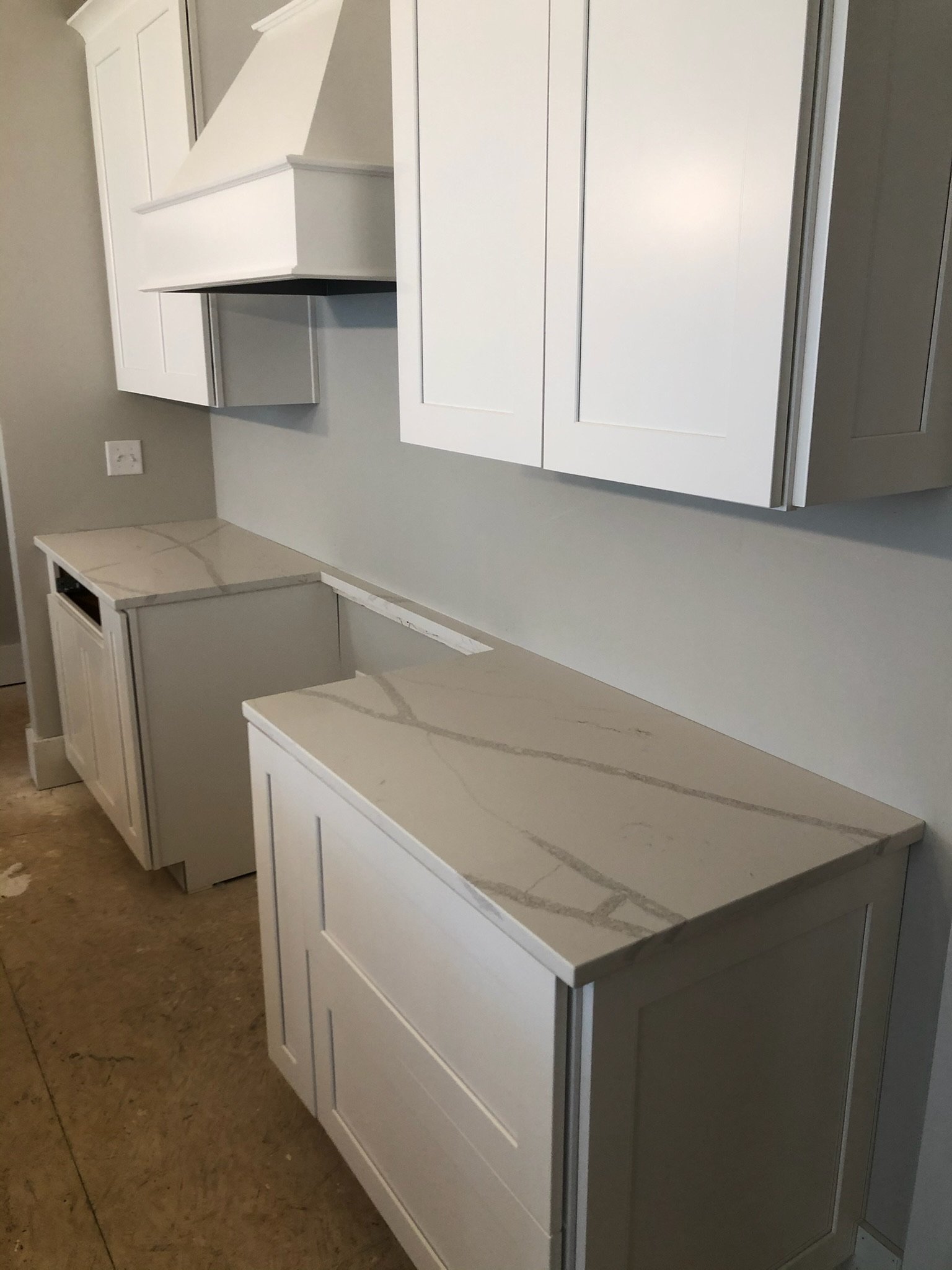 White kitchen cabinets with a marble countertop, some with doors, some without, against a beige wall with a power outlet.
