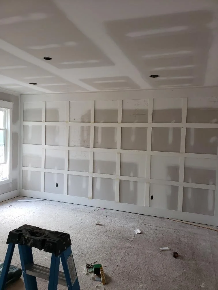 Room under construction with drywall partially installed on walls and ceiling, electrical outlets not yet installed, and construction tools on the floor.
