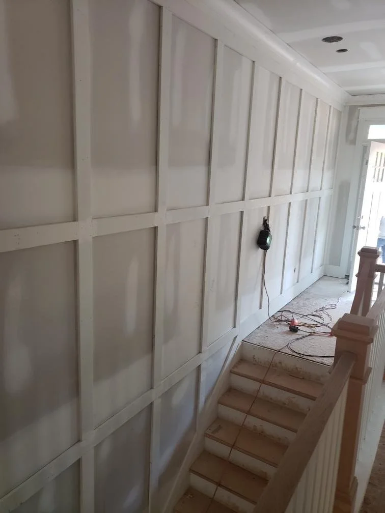 Interior wall under construction with exposed framing, stairs, and a partially finished ceiling. A small work light is hanging on the wall.