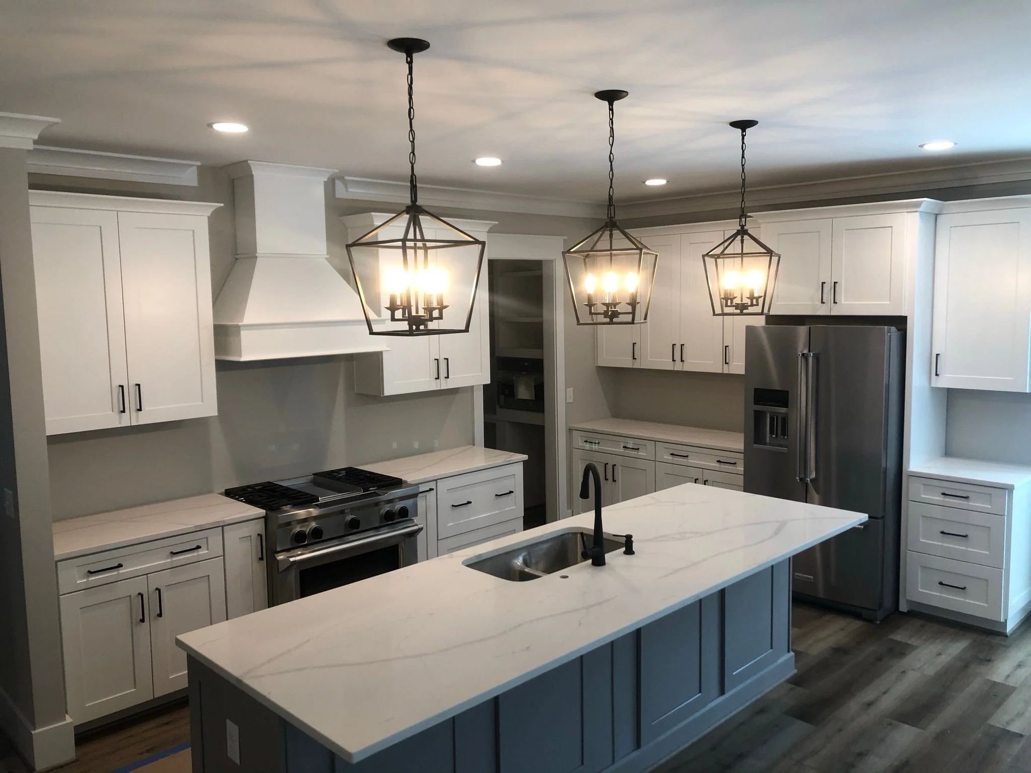 Modern kitchen with white cabinets, stainless steel refrigerator, marble island, black fixtures, and geometric pendant lights.
