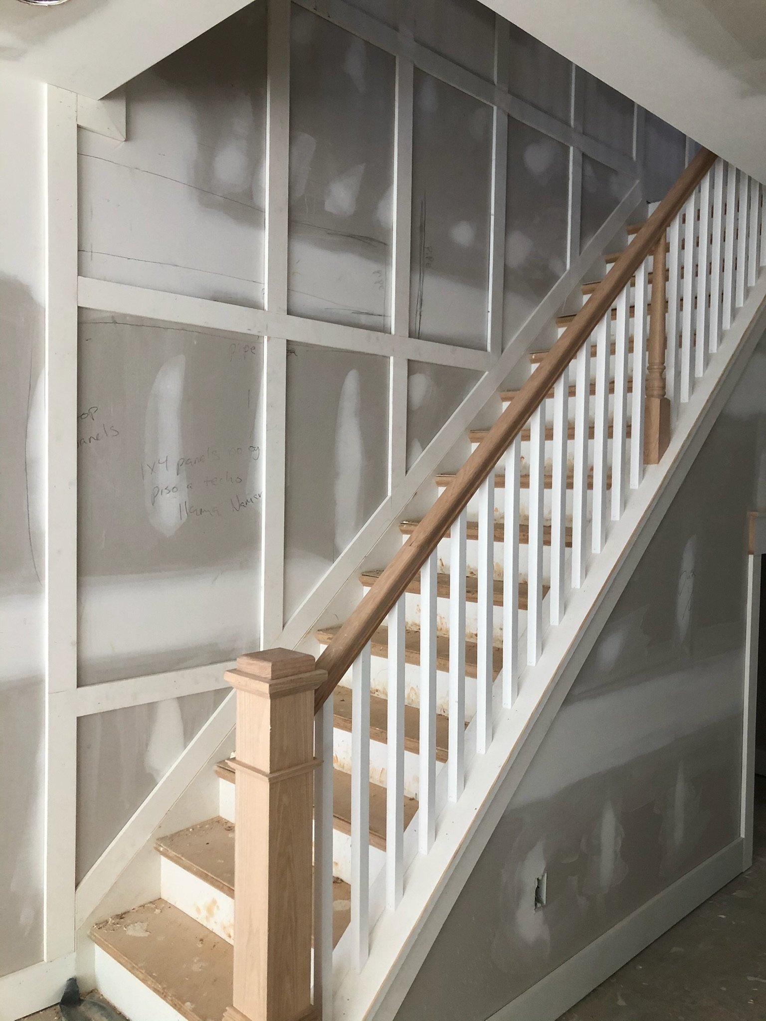 Inside view of staircase under construction, showing wooden handrail and white railing, with drywall walls behind.