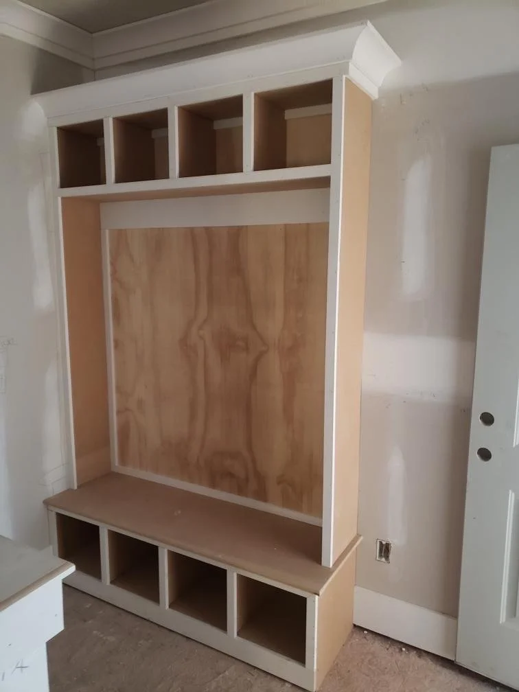 Unfinished custom built-in storage unit with open cubbies at the top, a large central space, and smaller compartments at the bottom, in a room under construction.