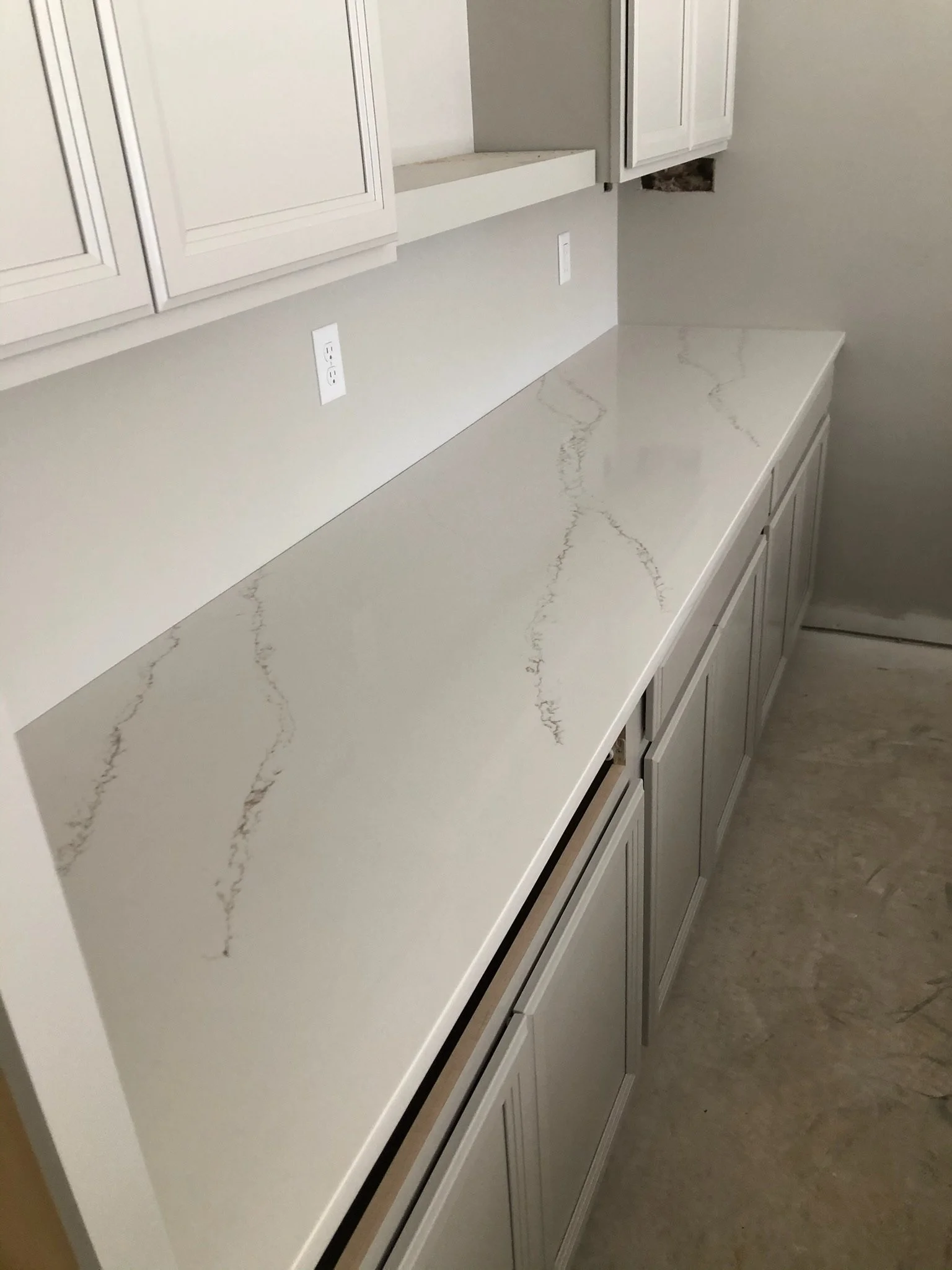 Close-up of a white kitchen countertop with subtle gray veining, white cabinets below, and two electrical outlets on the wall above.