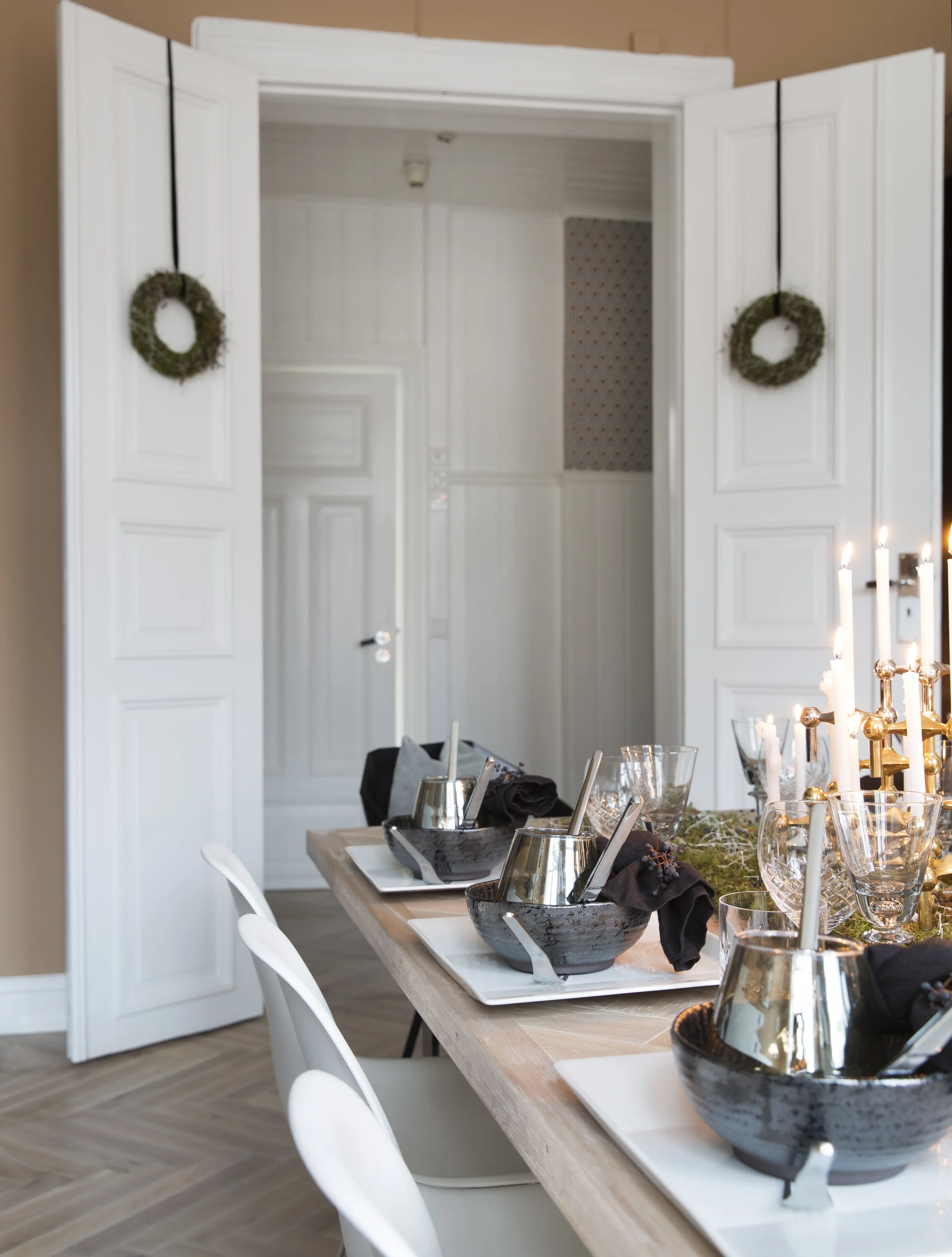 Små kranser hengt i svart silkebånd skaper julestemning på et blunk. Kransene er fra Frøken Flood Blomster. Alt listverk og alle karmer og dører er malt i klassisk hvit med høy glansgrad. Det gir et eksklusivt uttrykk som kler den gode takhøyden.