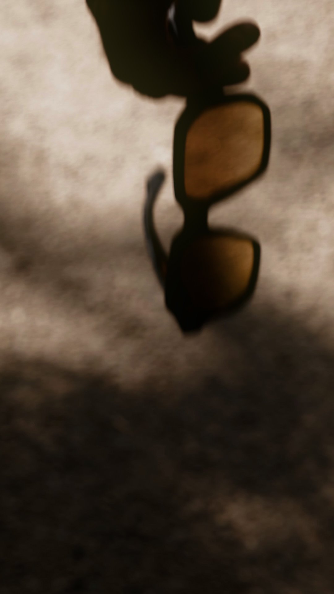 HUG Spectacles DUPREE sunglasses held in soft sunlight, highlighting the geometric frame and tinted lenses.