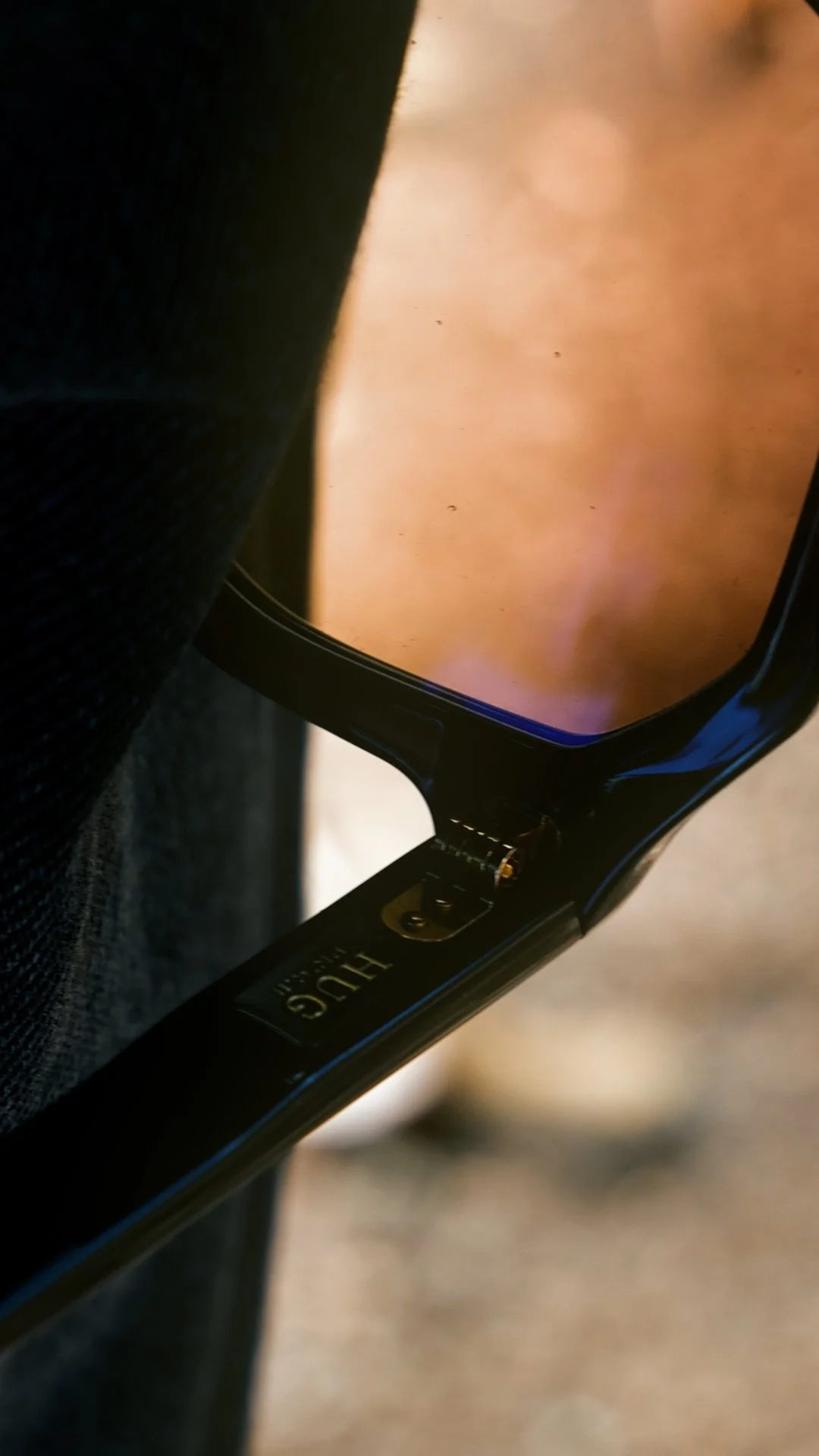 Detail of the HUG Spectacles DUPREE frame, showing the black acetate, hinge and engraved HUG branding.