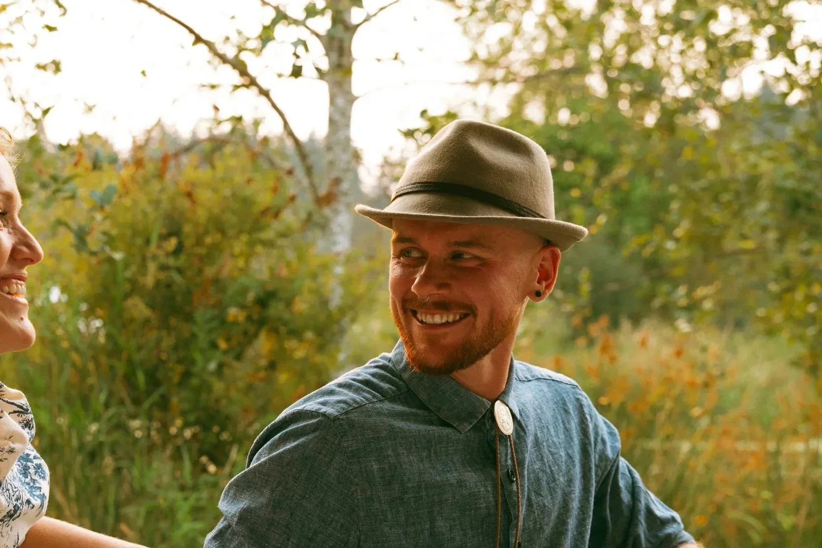 August Waite, counsellor in Victoria, a masculine non-binary person with a red beard, laughing and looking over their shoulder with trees in the background.