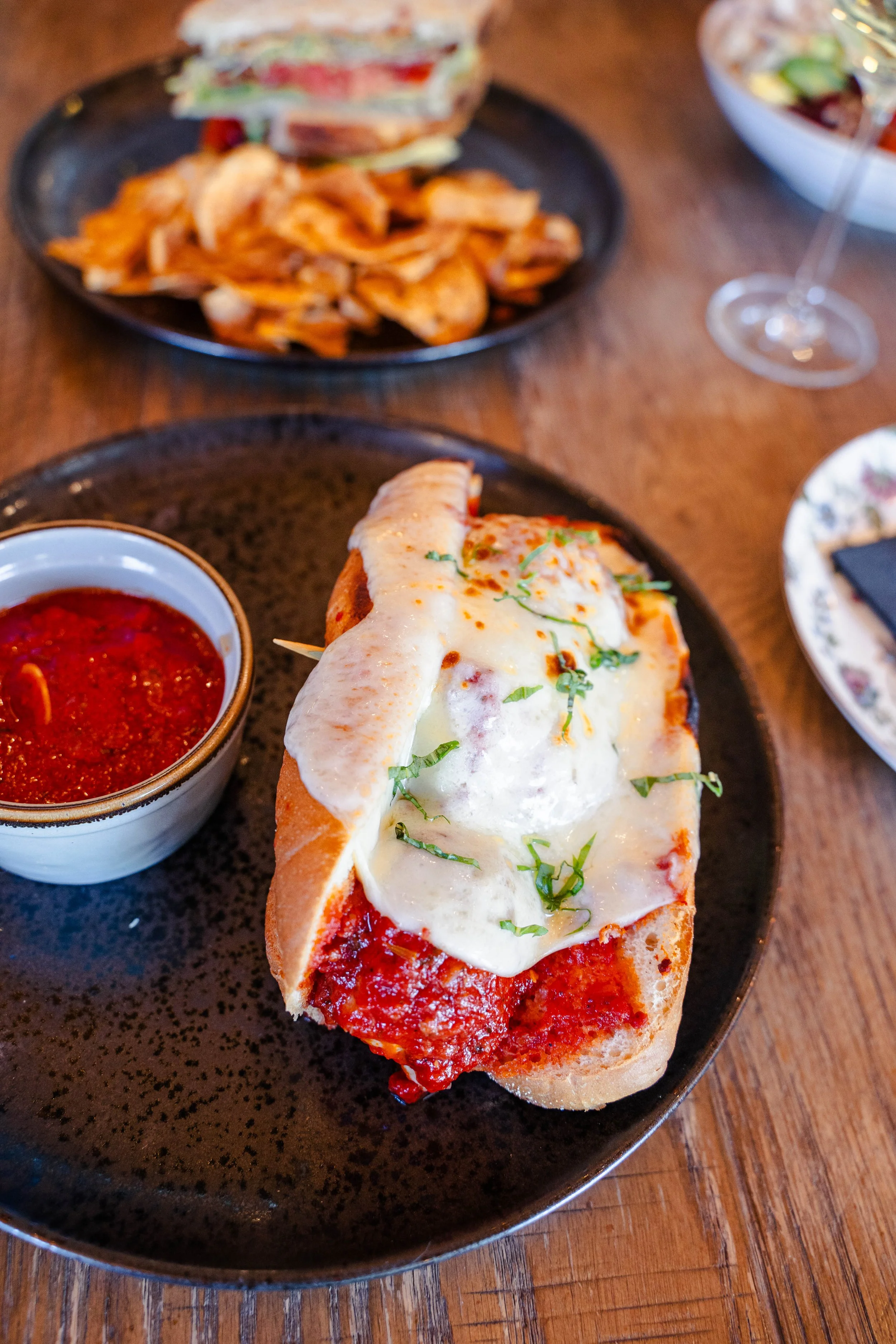 Meatball sub piled high with our mom’s family meatball recipe and a side of marinara, with a classic BLT and chips in the background at Eddy’s Kitchen in downtown Aspen.
