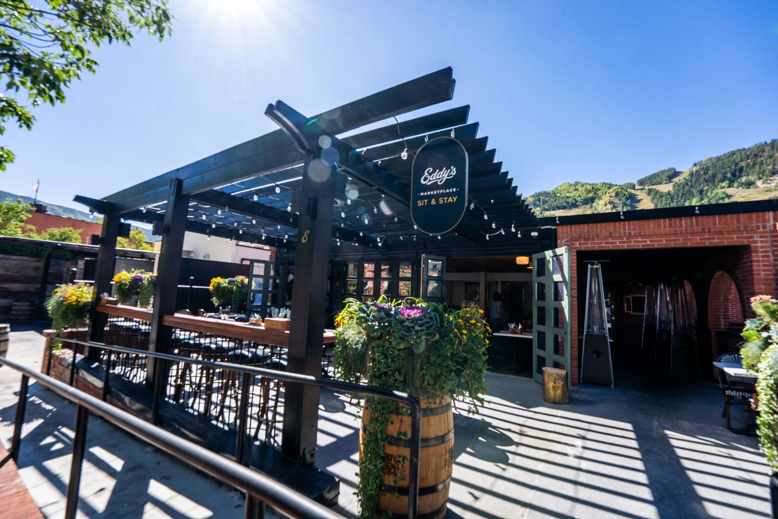 Sunlit outdoor patio and bar at Eddy’s Kitchen in downtown Aspen, featuring a cozy pergola and inviting space for private events, cocktail hours, celebrations, and outdoor dining.