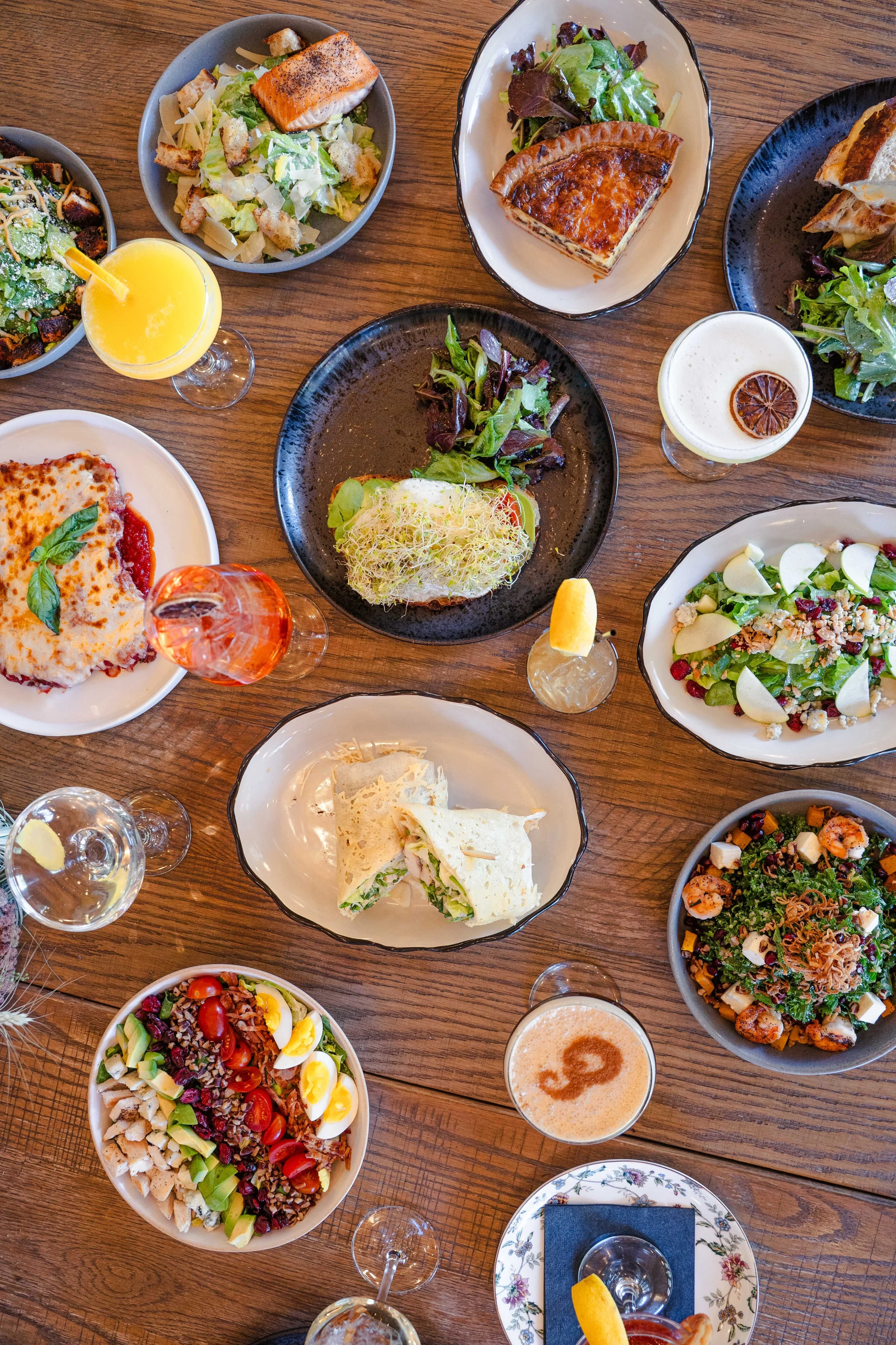 Table filled with signature dishes, cocktails, wine, and drinks from Eddy’s Kitchen – Sit & Stay, our restaurant and bar in downtown Aspen.”