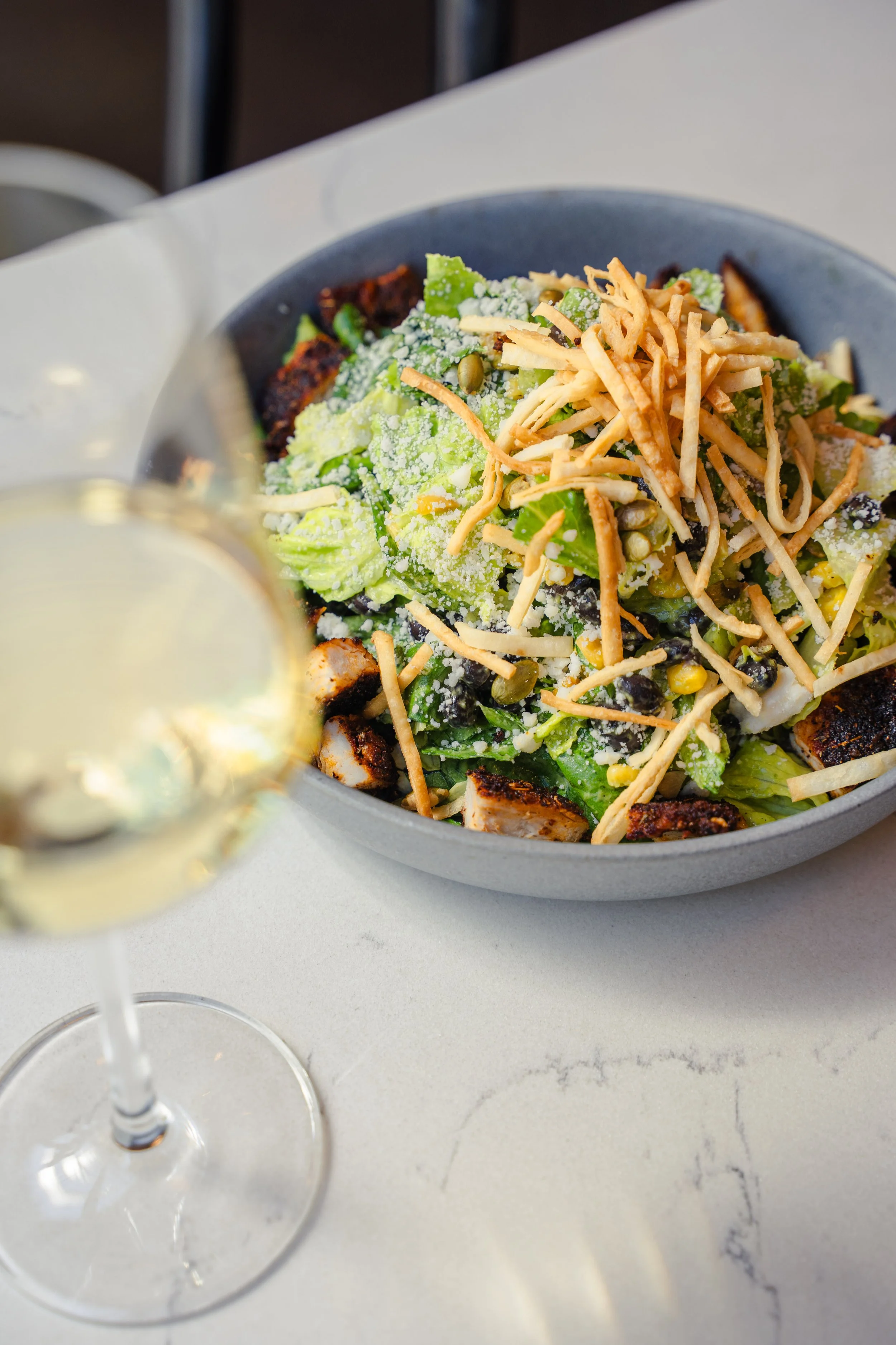 Southwestern salad piled high and paired with a glass of white wine on the patio at Eddy’s Kitchen, offering casual outdoor dining in downtown Aspen.