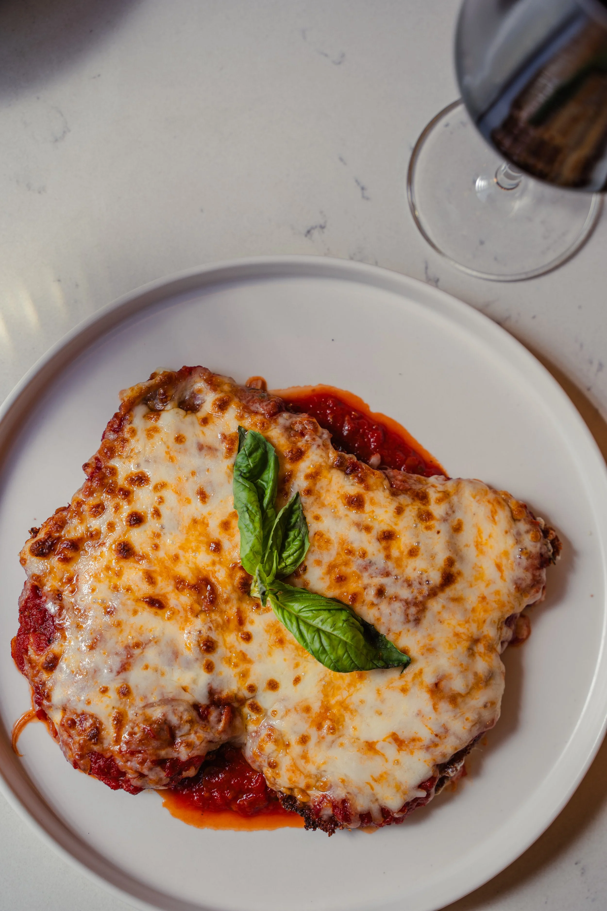 Classic chicken Parmesan topped with fresh basil and paired with a glass of red wine at Eddy’s Kitchen, a cozy casual restaurant in downtown Aspen.
