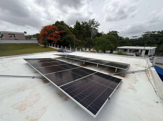Solar panels mounted on a flat rooftop, with trees and cloudy sky in the background.