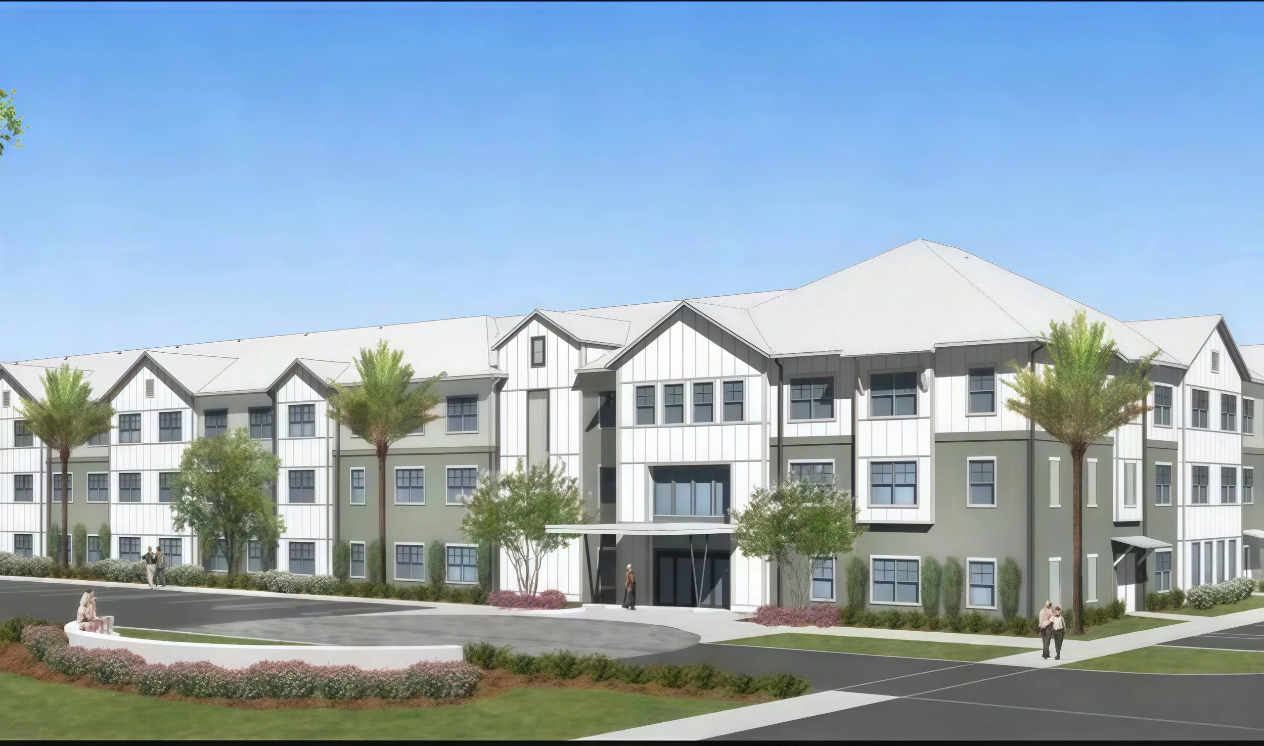 A modern multi-story apartment building with white and gray exterior, multiple windows, and some trees in front. Several people are walking or sitting nearby on a landscaped area with bushes and flower beds under a clear blue sky.