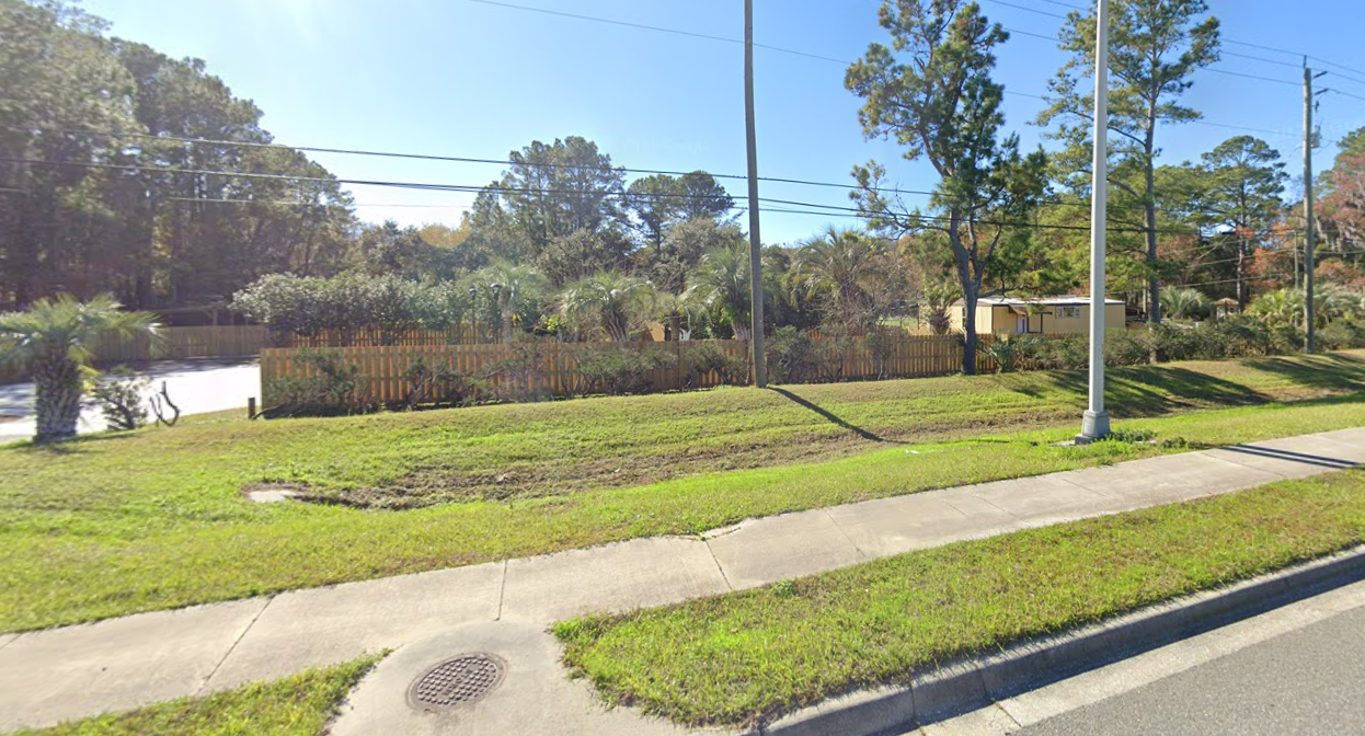 A sidewalk alongside a grassy area with a lamppost and trees. A backyard with a wooden fence and trees is visible in the background.