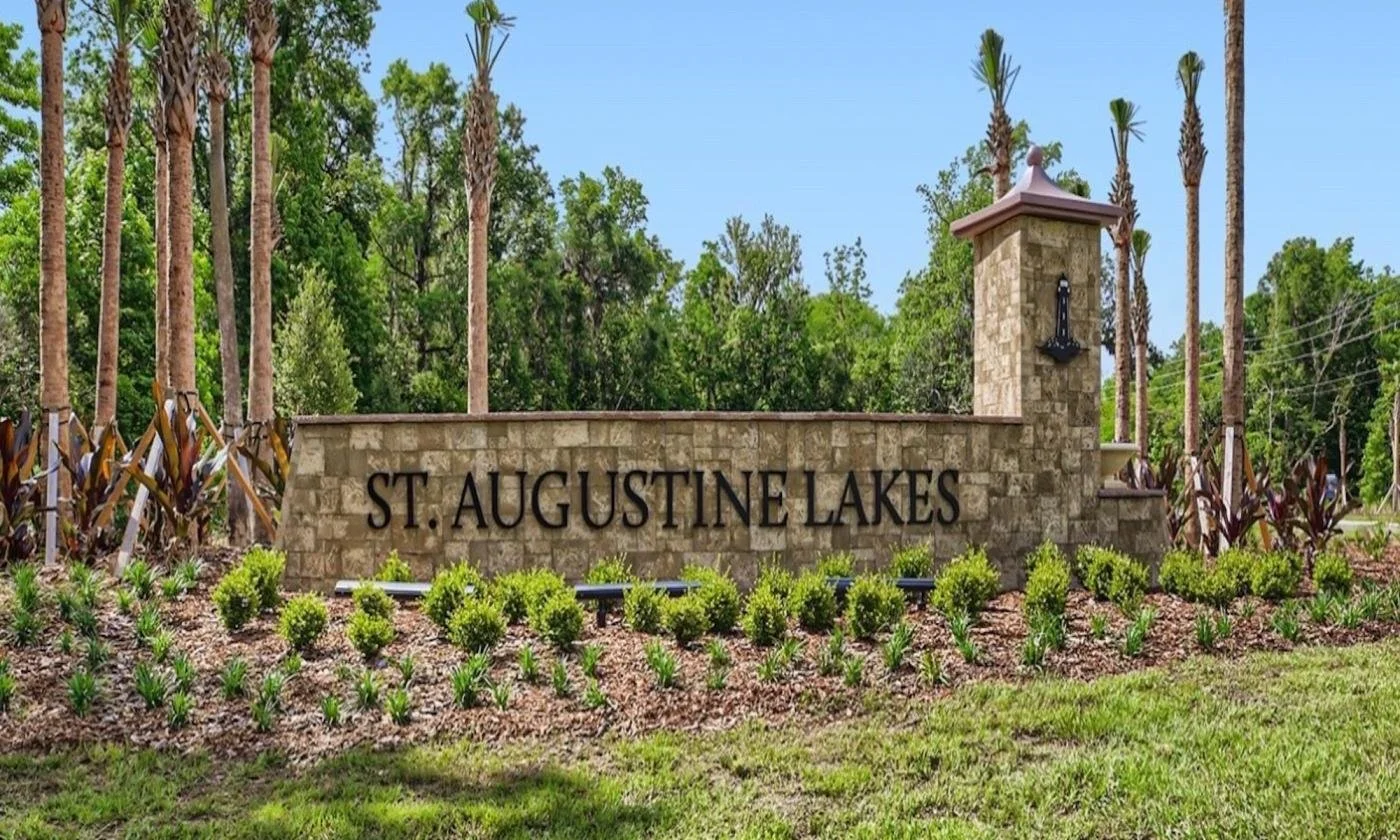 Entrance sign for St. Augustine Lakes with stone wall, greenery, and tall palm trees in the background.