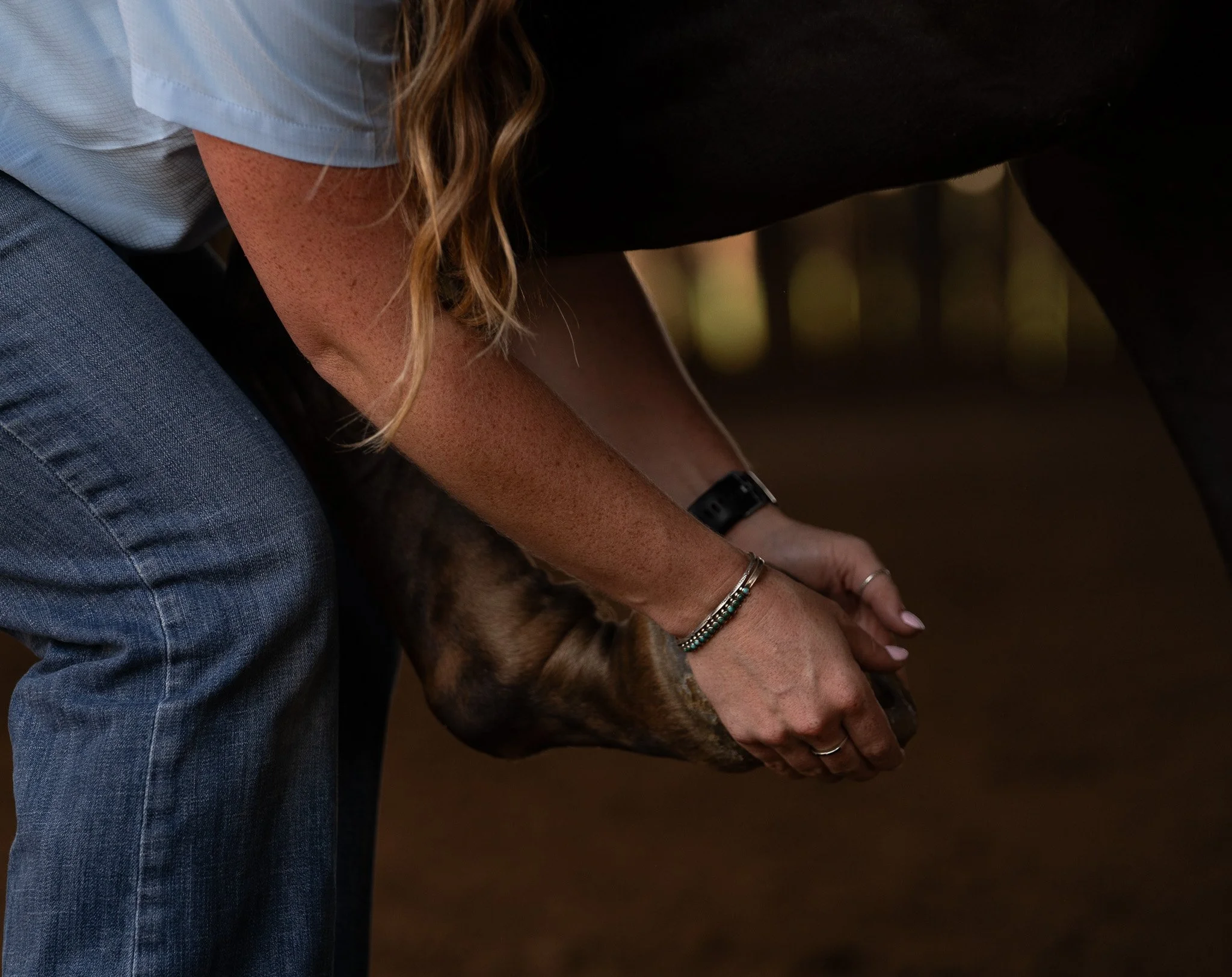 A person with curly hair wearing a bracelet and a watch, holding a dog with a patterned coat, on a dark background.
