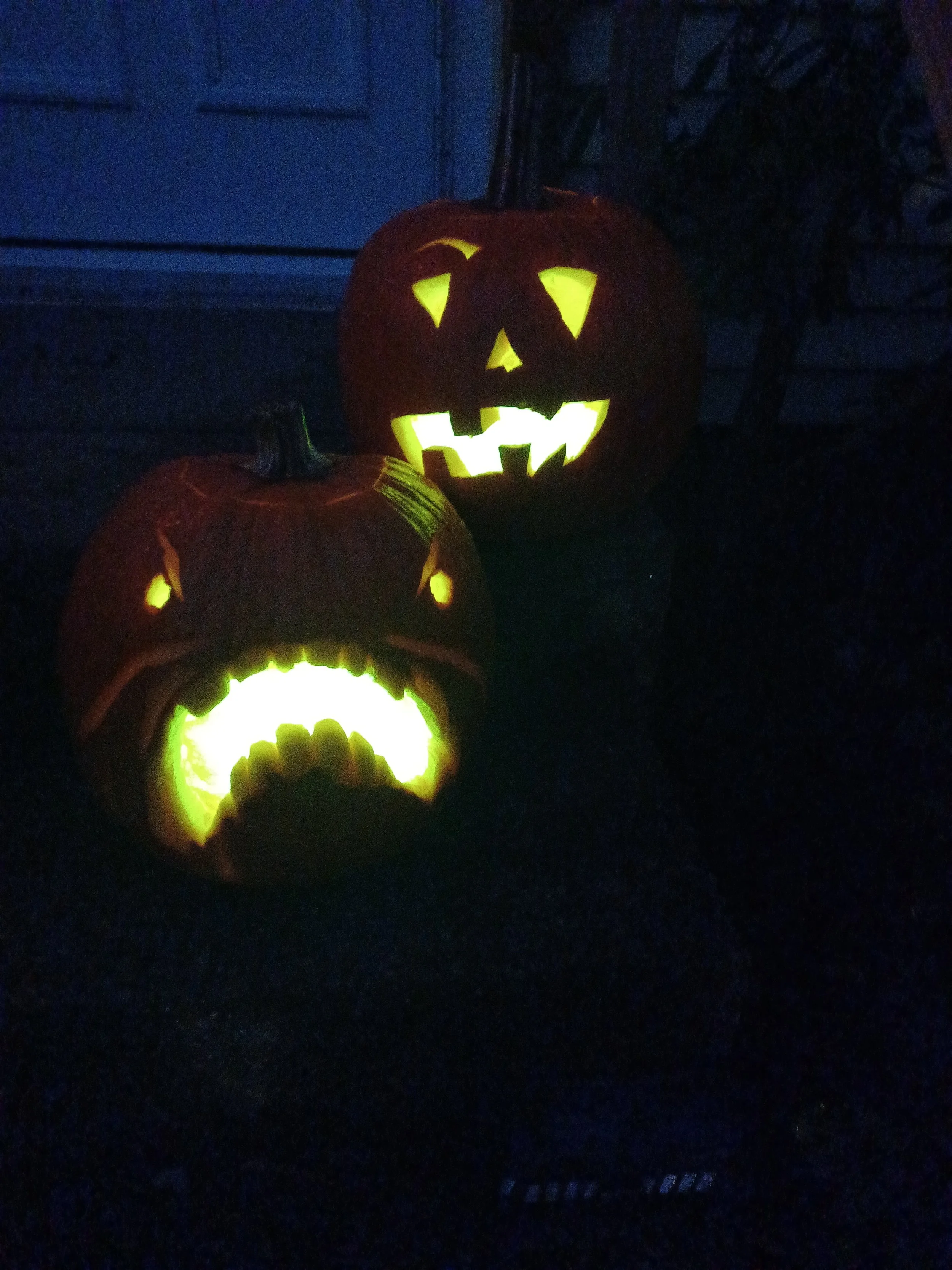 Two carved pumpkins with glowing faces in a dark setting, Halloween decorations.