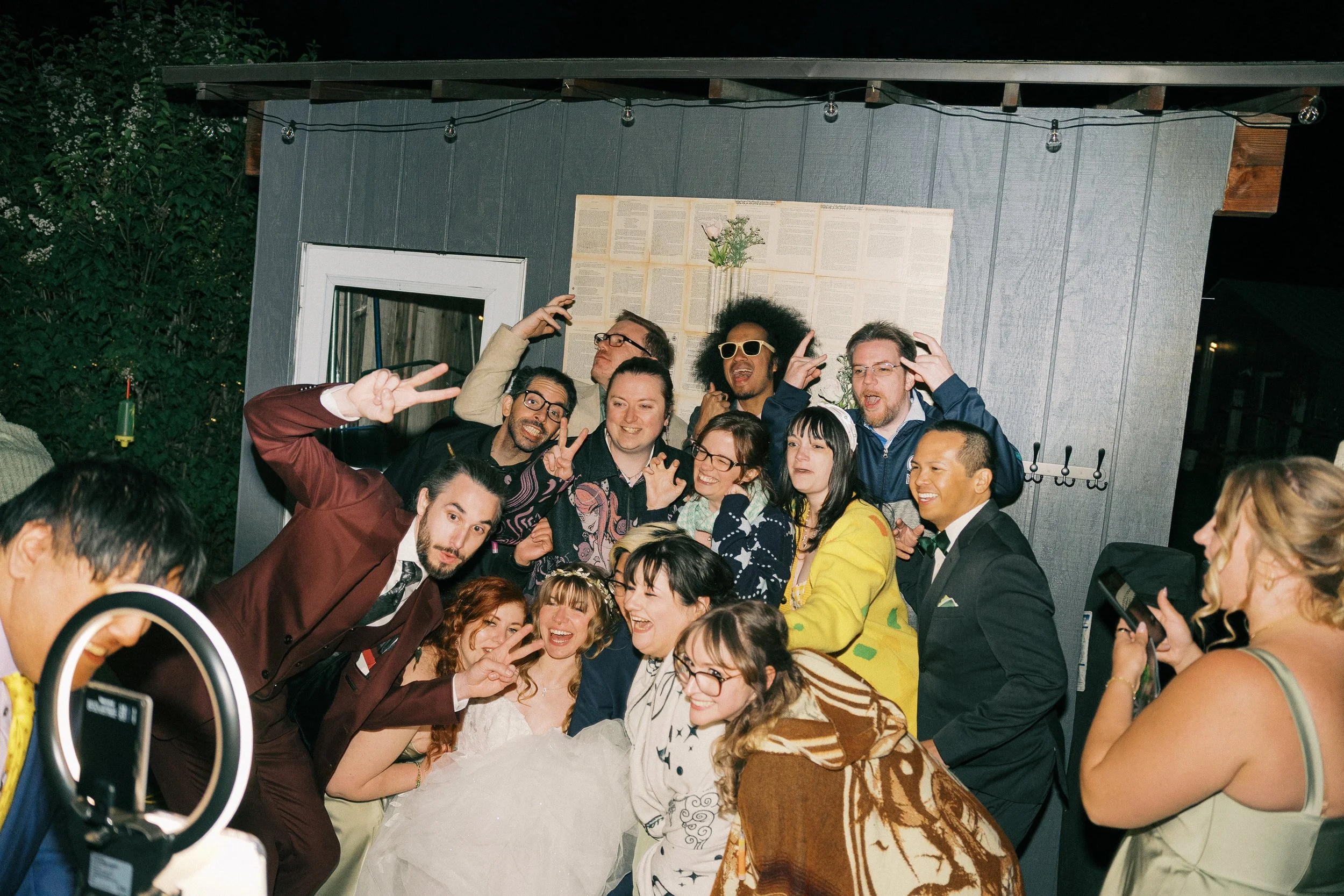 Large group posing and smiling at an outdoor wedding reception under string lights
