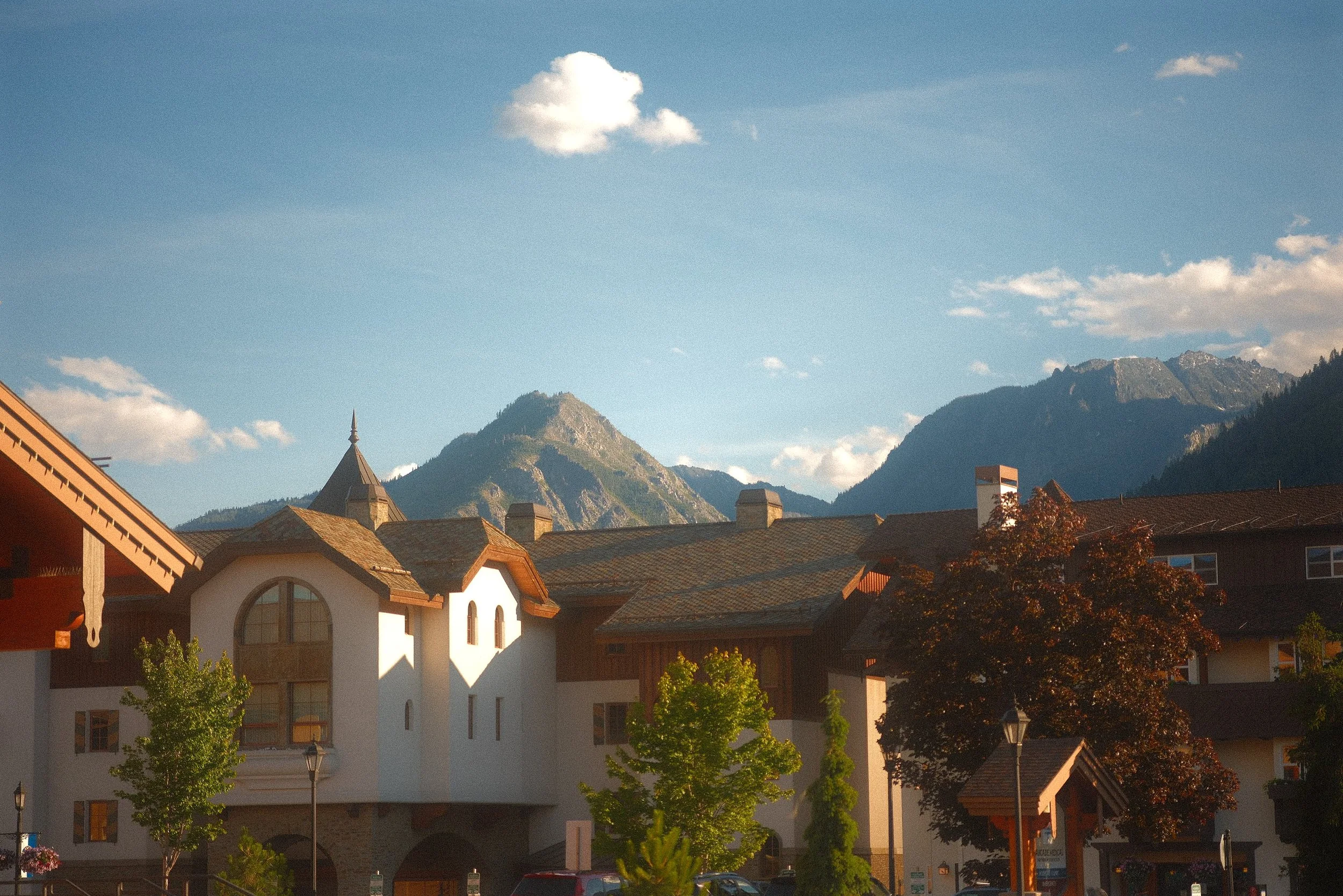 Alpine village with a church, traditional buildings, and dramatic mountain peaks under a blue sky
