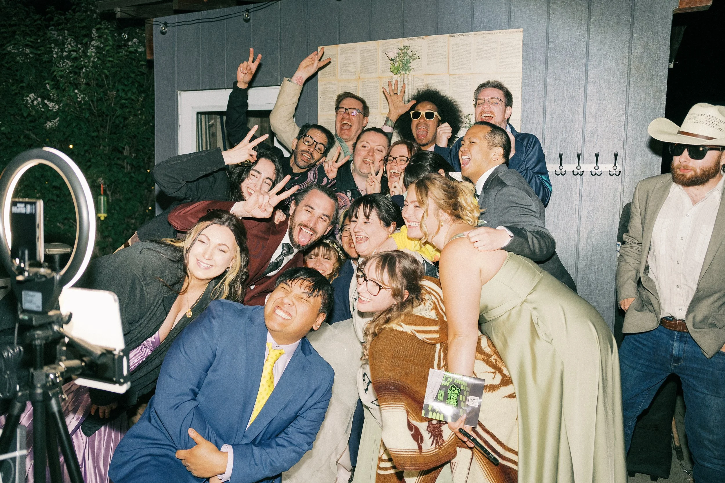Large group of smiling people posing for a fun party photo beside a ring light outdoors