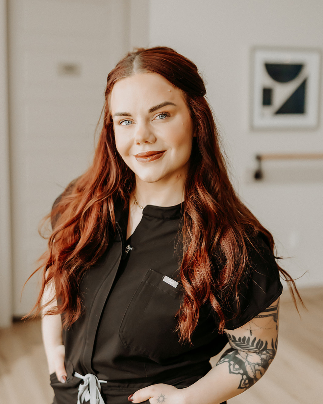 woman with red hair in black scrubs smiling