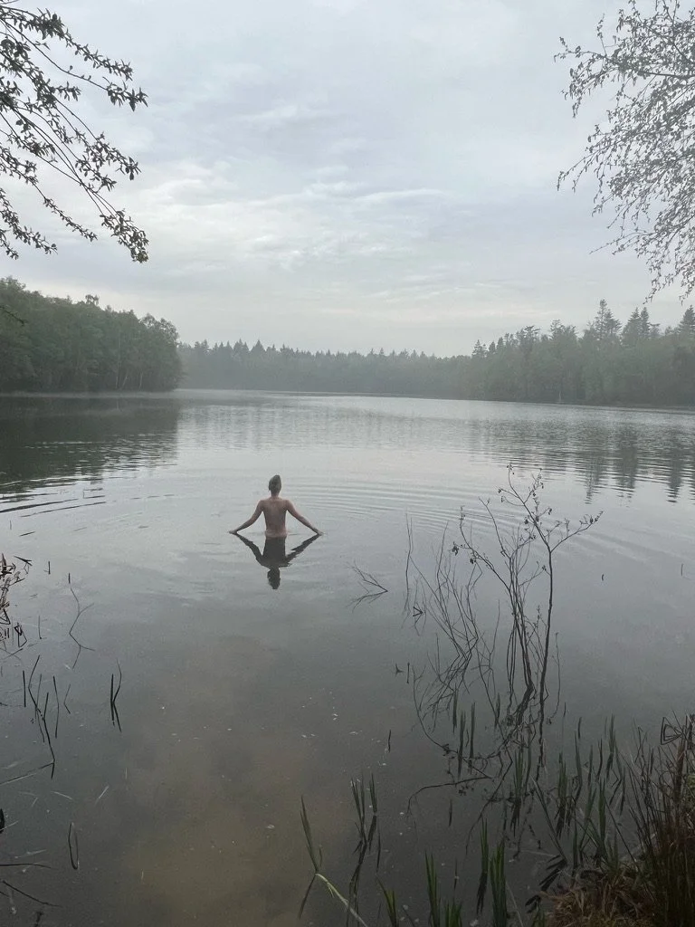 Persoon die rust in een kalm meer met omliggende bomen, onder een bewolkte hemel.